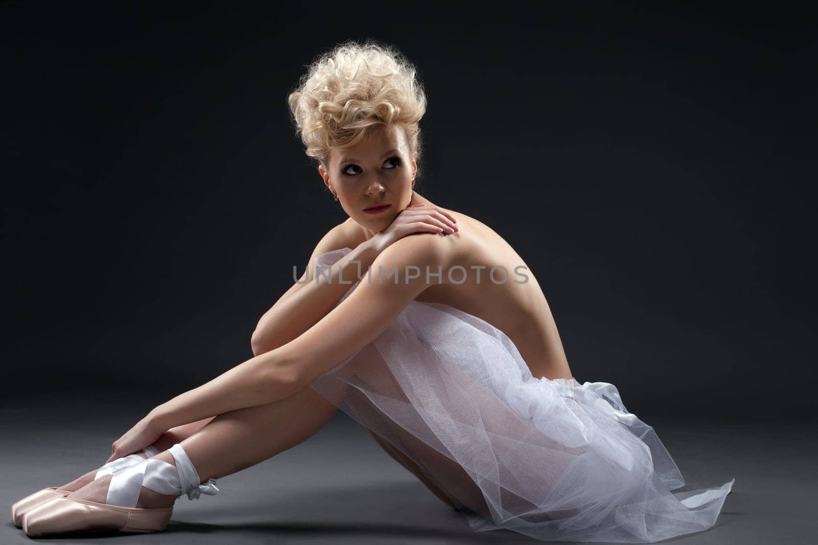 Shot of curly blonde ballerina posing in studio, on gray background