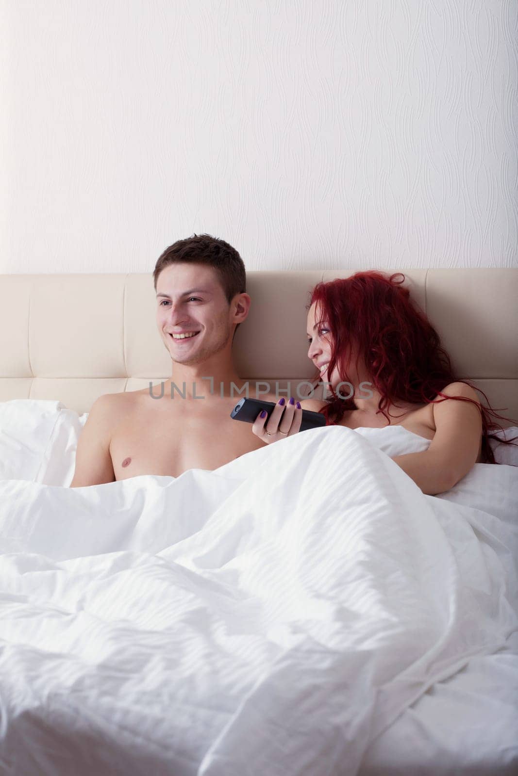 Happy young couple watching TV while lying in bed, close-up