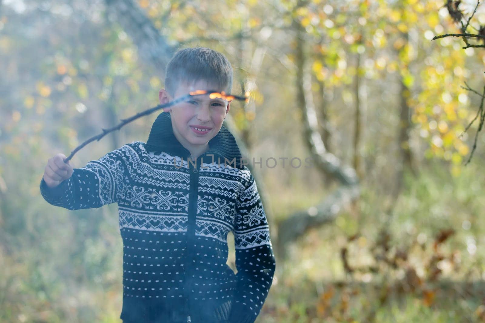 The boy is holding a burning wooden branch.