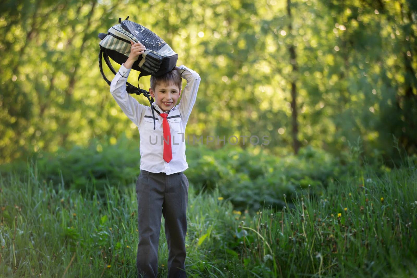 A happy schoolboy with a briefcase walks from school through a green park. by Sviatlana