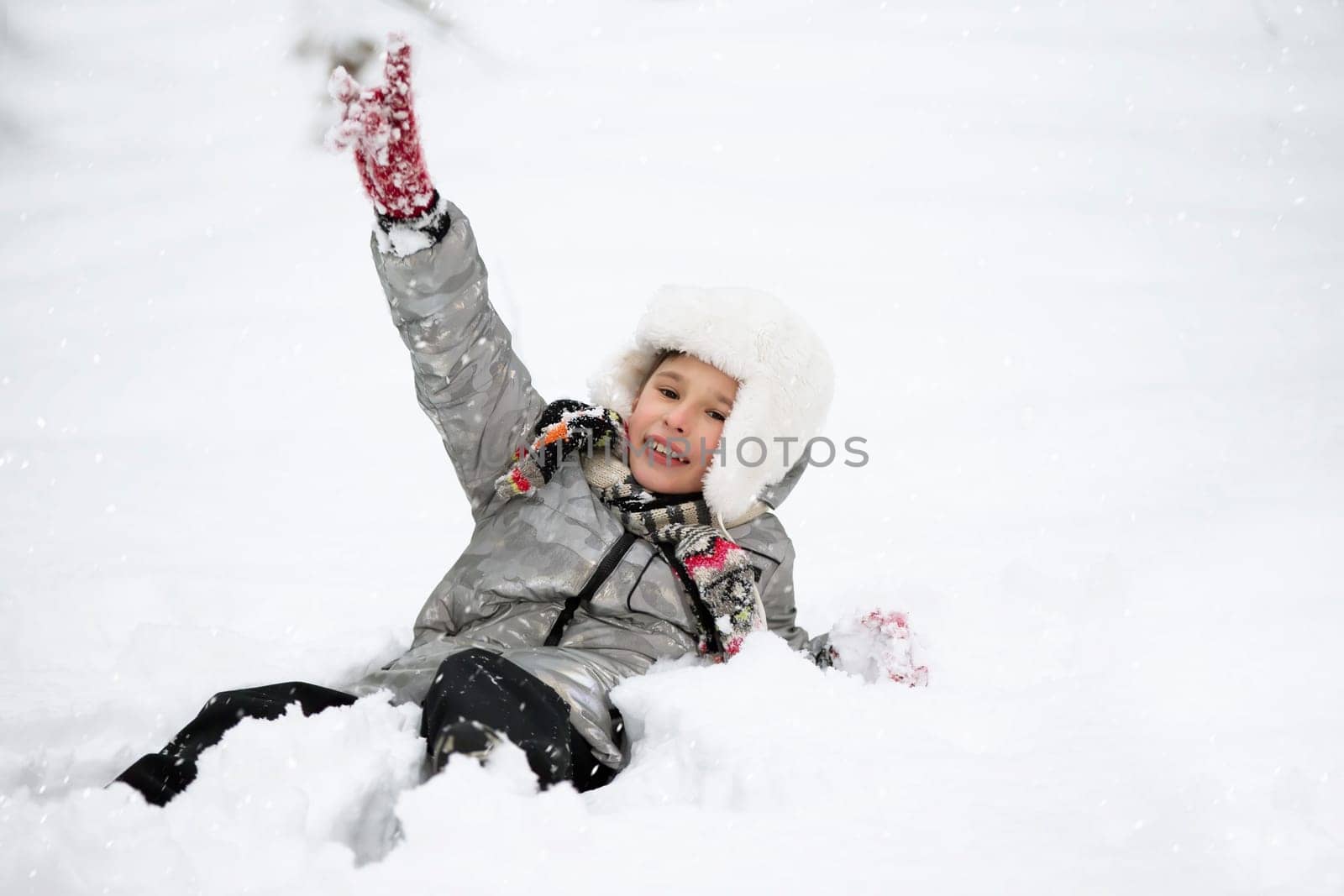 A joyful boy in warm clothes lies in the snow. Child on a winter walk.