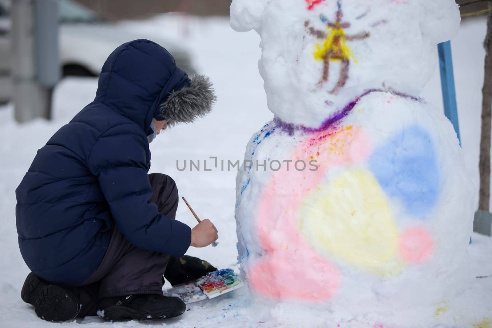 A boy paints a snowman on a winter day.