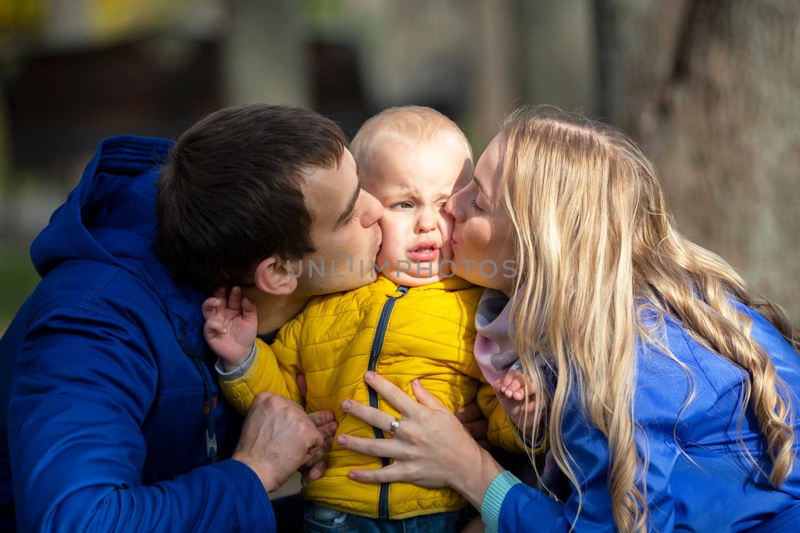 Happy family mom dad and little son. A woman and a man kiss a small child. by Sviatlana