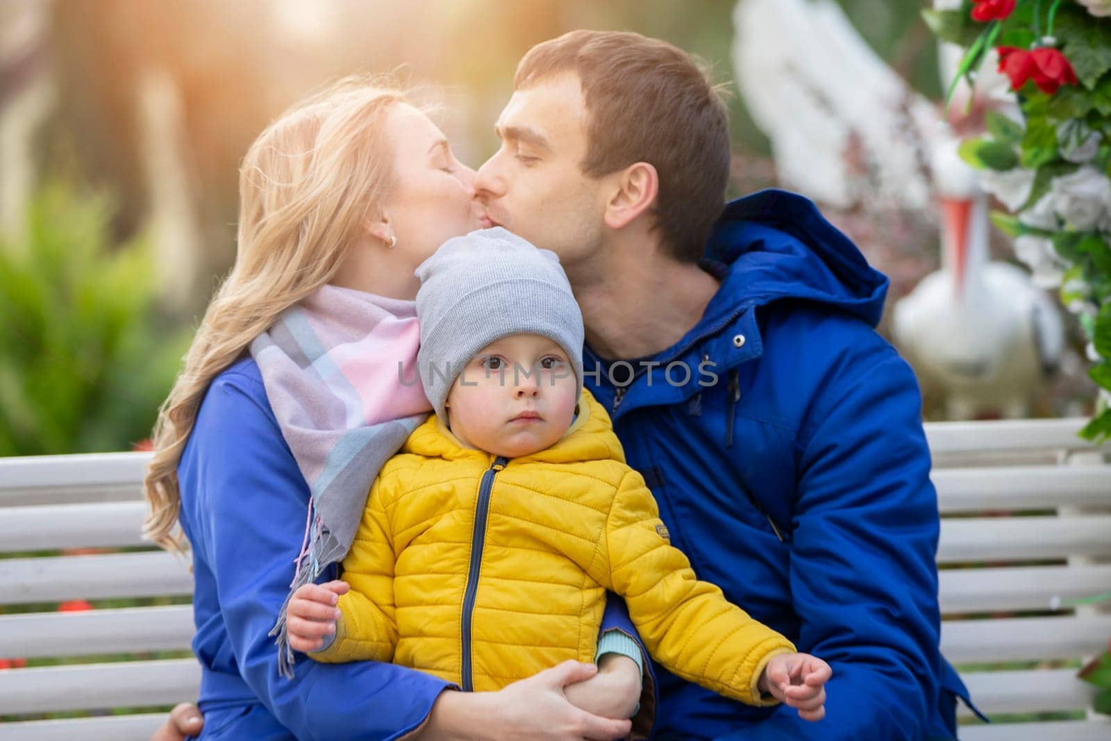 Happy family mom dad and little son. A woman and a man kiss and hold a small child in their arms.