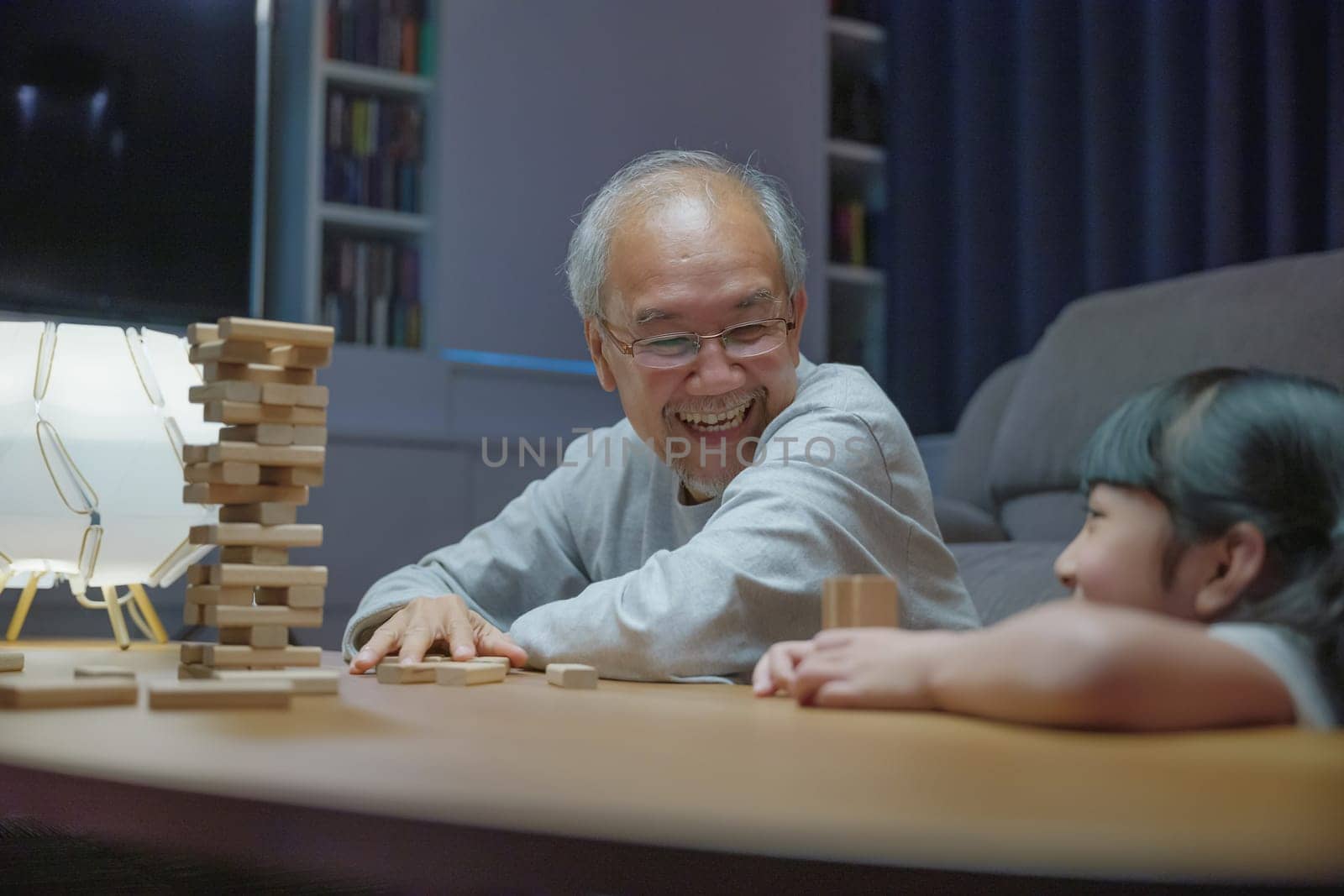 Happy grandparents Asian family enjoy playing toy block with little daughter and mother together at home night time, Smiling parent having fun play build constructor tower of wooden blocks, education