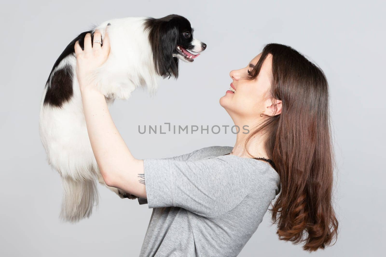 A cute young woman is hugging her papillon puppy. Love between owner and dog. Girl with dog studio portrait.
