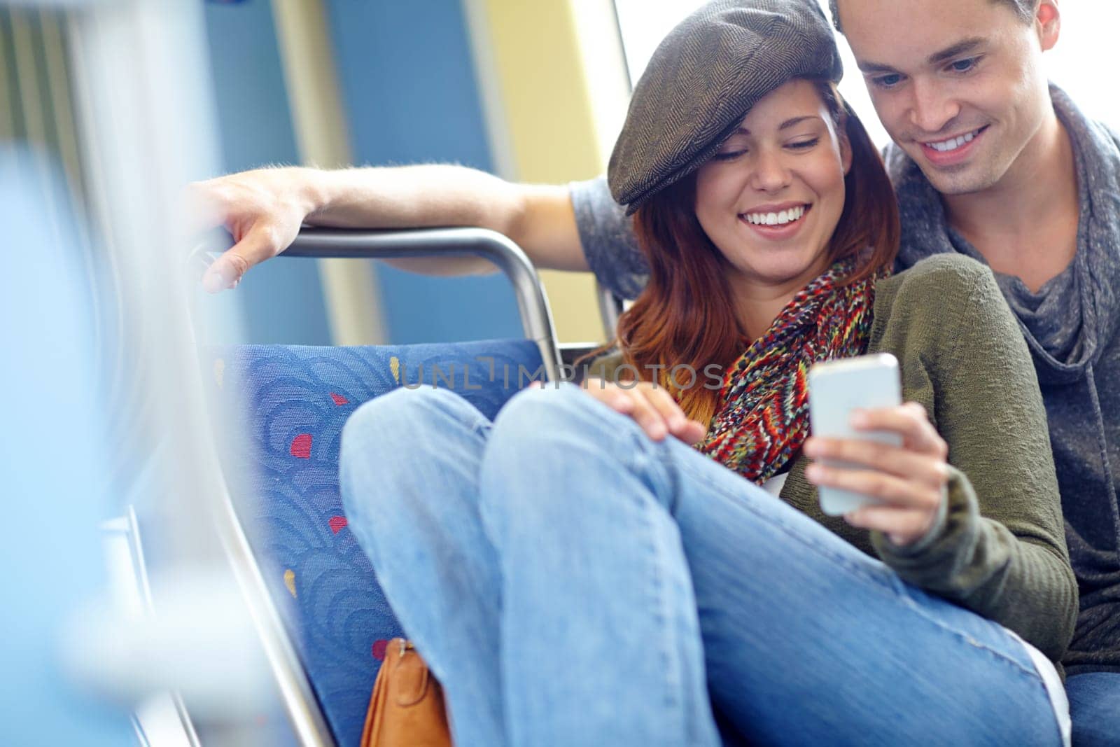Technology bringing people closer together. a happy couple on the train looking at something on a cellphone. by YuriArcurs
