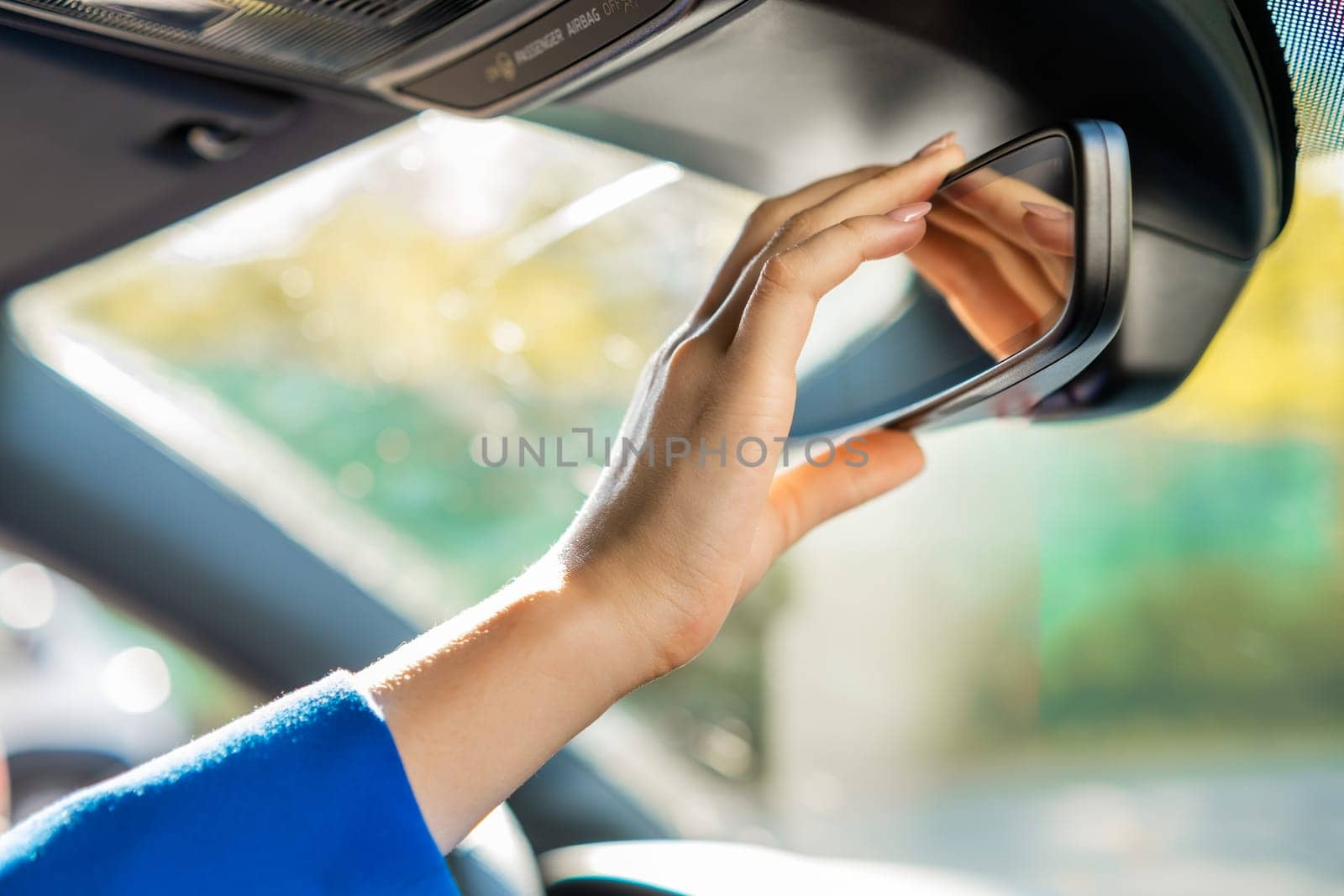 Close up womans hand adjusting the rearview mirror sitting in the car.