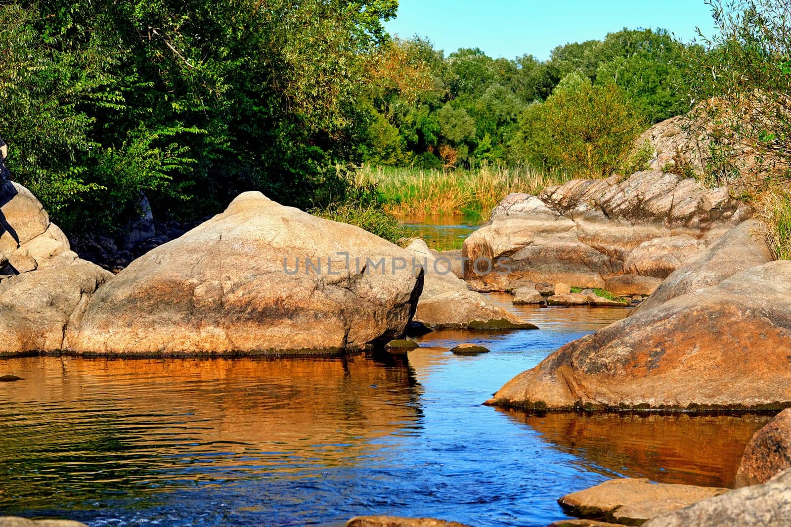 a large natural stream of water flowing in a channel to the sea, a lake, or another such stream. Peaceful calm river among big stones and green meadows with trees