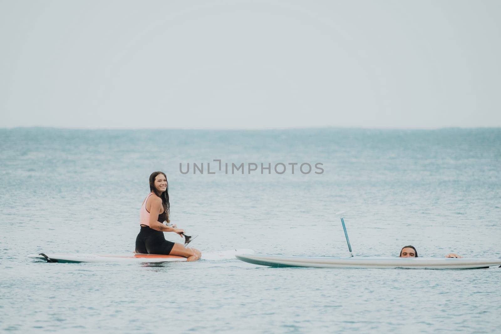 Sea woman and man on sup. Silhouette of happy young woman and man, surfing on SUP board, confident paddling through water surface. Idyllic sunset. Active lifestyle at sea or river