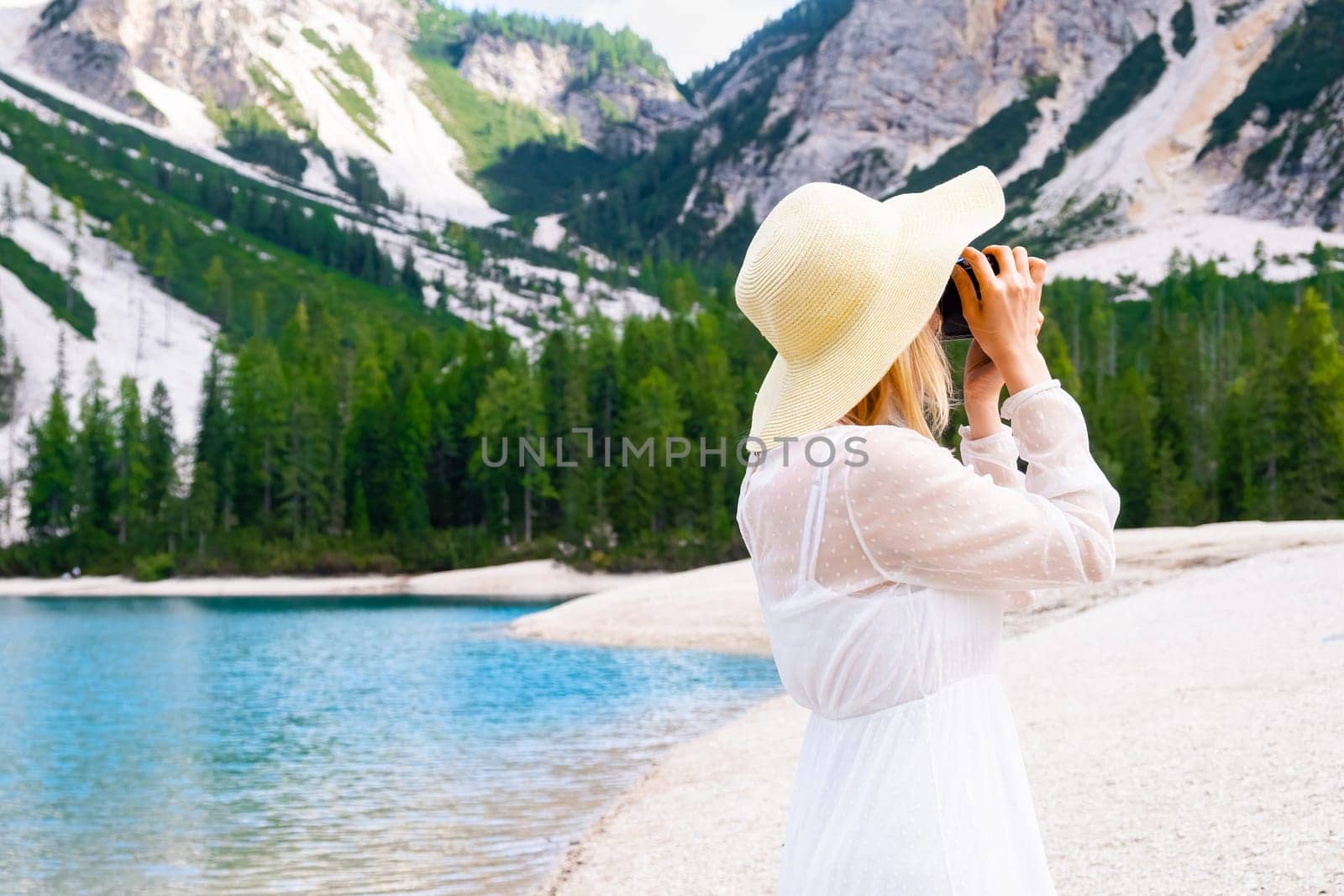 Blonde hair female photographer in straw hat and white dress taking pictures of Dolomites near Lake Braies with copy space