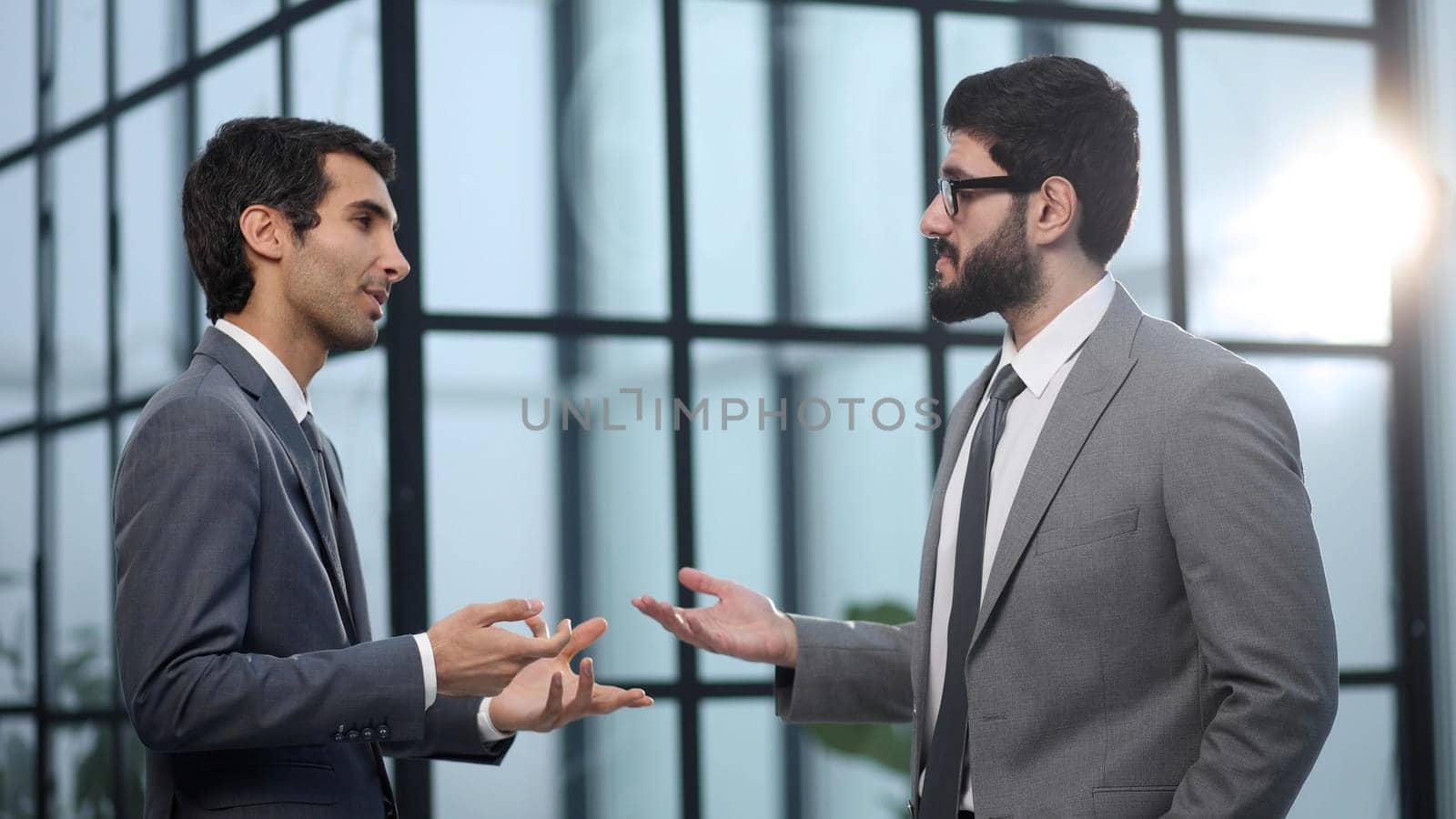 Business executive man and colleague standing in modern office hallway discussing project.