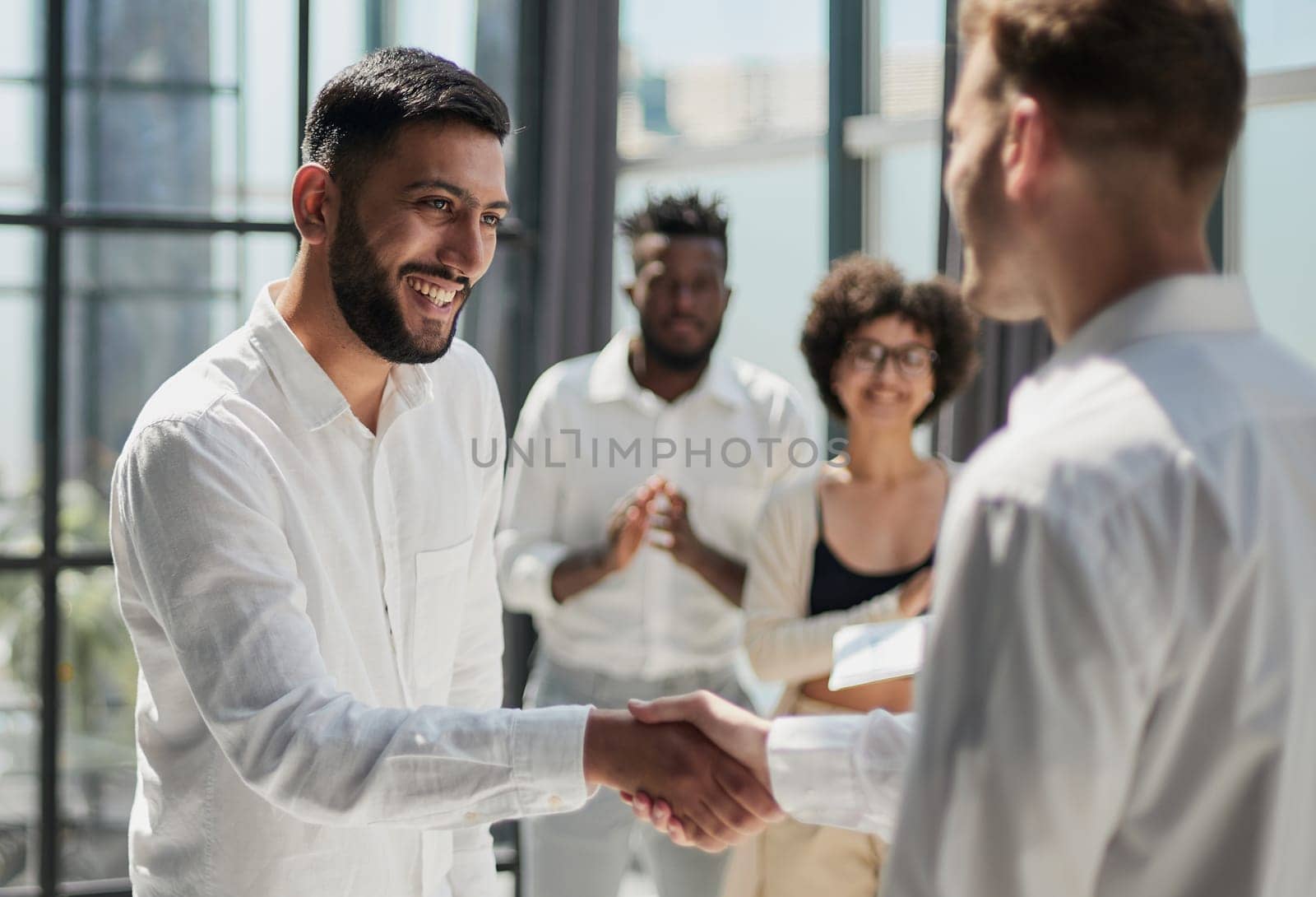 Glad to work with you. Young modern men in smart casual wear shaking hands and smiling while working in the creative office