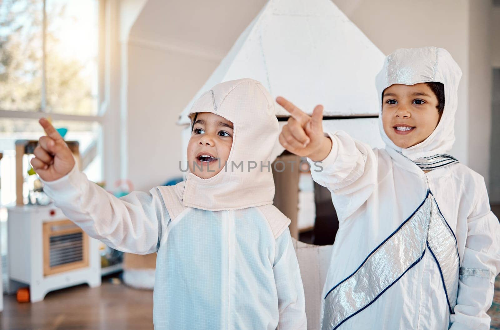 Astronaut, home and children pointing, playing and role play space travel, fantasy games or explore new discovery. Rocket spaceship, creative halloween costume and kids imagine a galaxy adventure by YuriArcurs