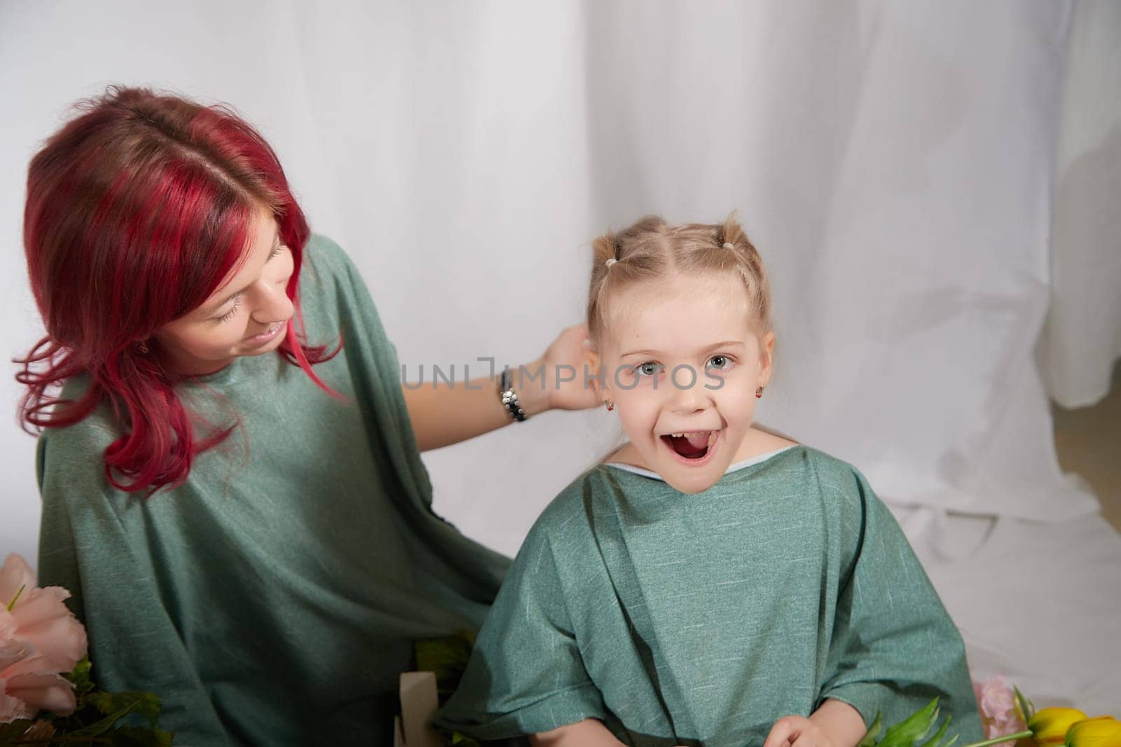 Amazing pretty mother and daughter having fun with flowers in 8 March or in Mother's day. Red haired mom and small little blonde girl having lovely free time on white background by keleny