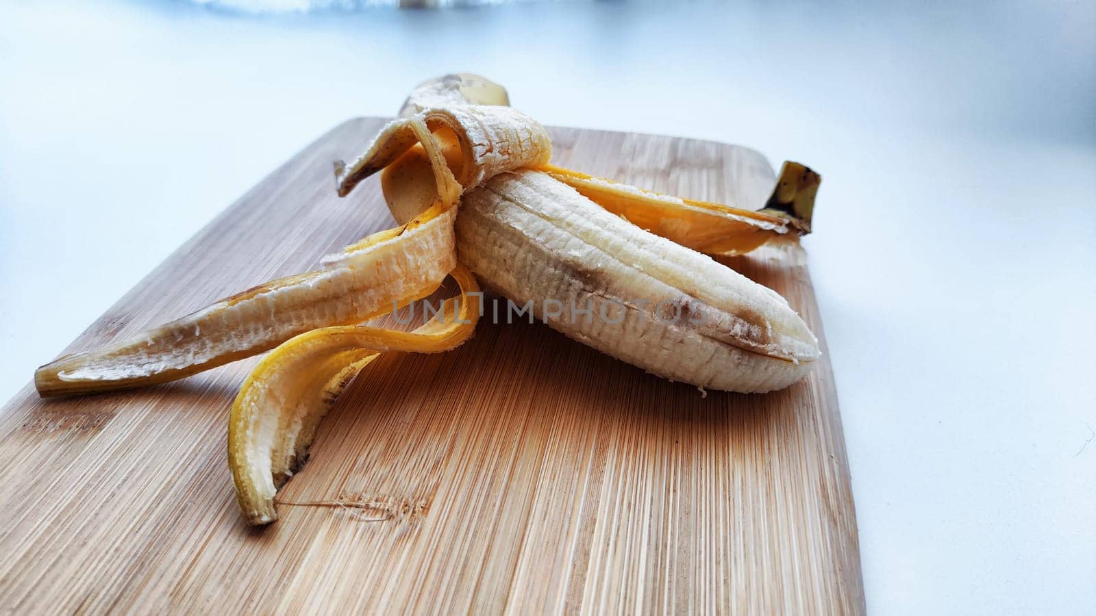 Banana with open peel on wooden board and white background. Ripe banana with peel, Close up. Delicious sweet fruit dessert