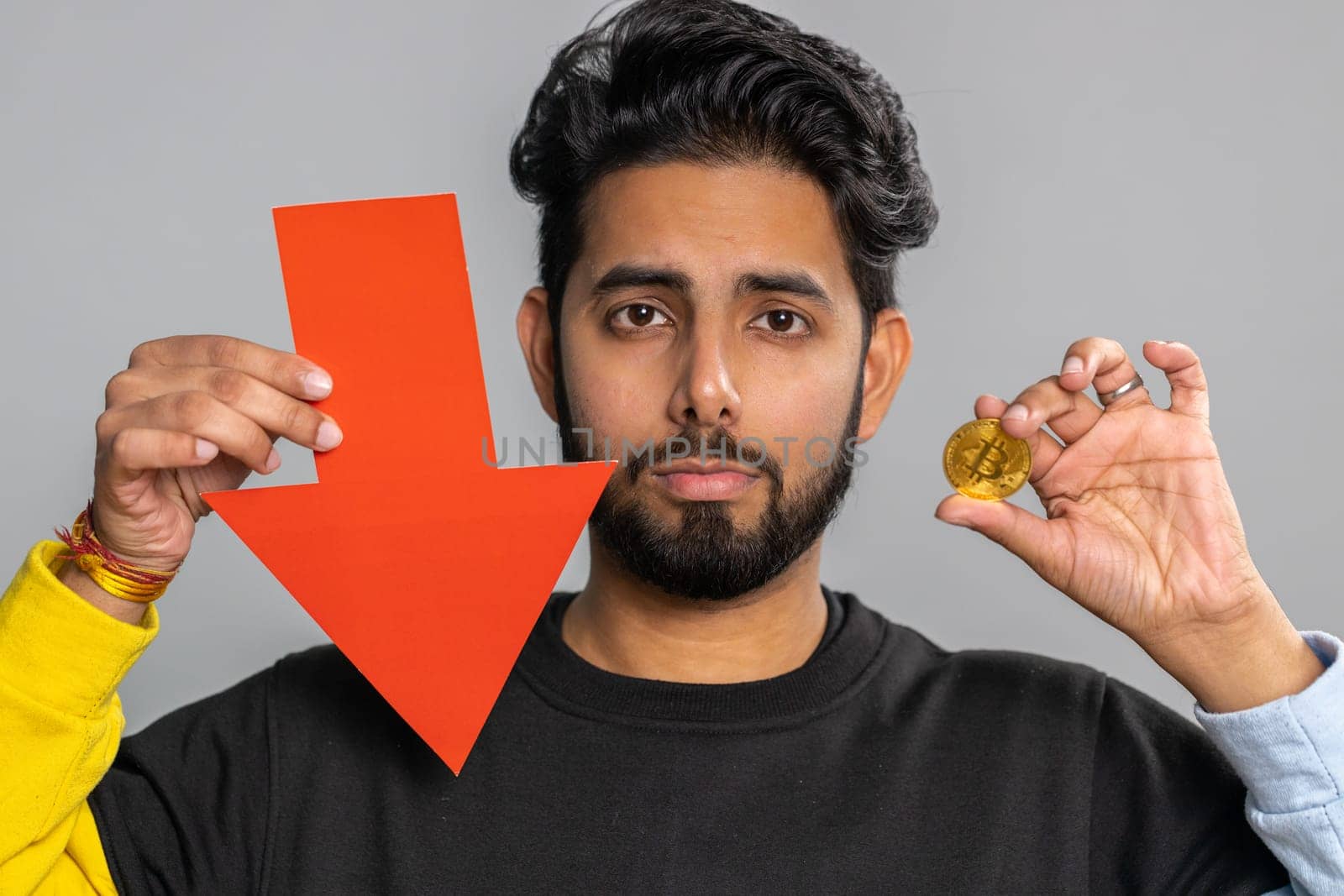 Upset indian man showing red arrow pointing down, downgrade, unsuccessful business, fall of cryptocurrency stock market investment, mining bitcoins BTC money exchange rate, bankruptcy fail. Hindu guy