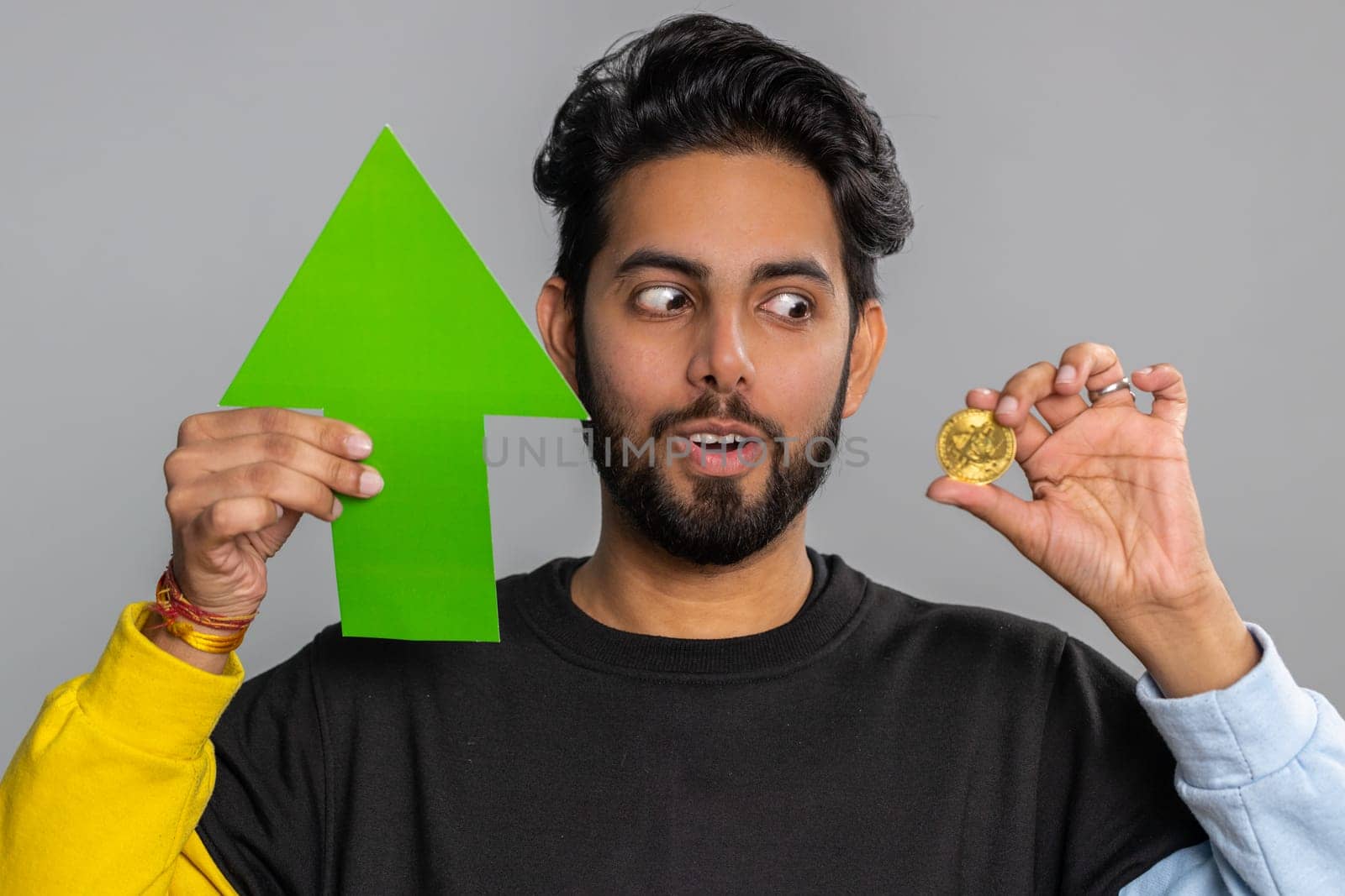 Indian man winner holding arrow sign pointing up showing golden bitcoins, cryptocurrency investment, mining BTC money exchange increase. Hindu guy showing up indicating successful development progress
