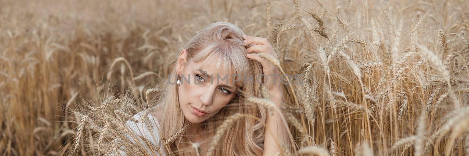 A blonde woman in a long white dress walks in a wheat field. The concept of a wedding and walking in nature.