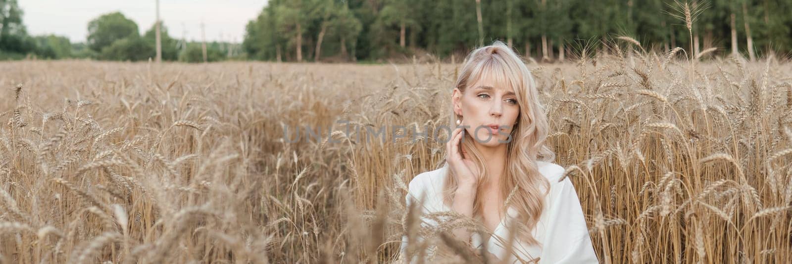 A blonde woman in a long white dress walks in a wheat field. The concept of a wedding and walking in nature.