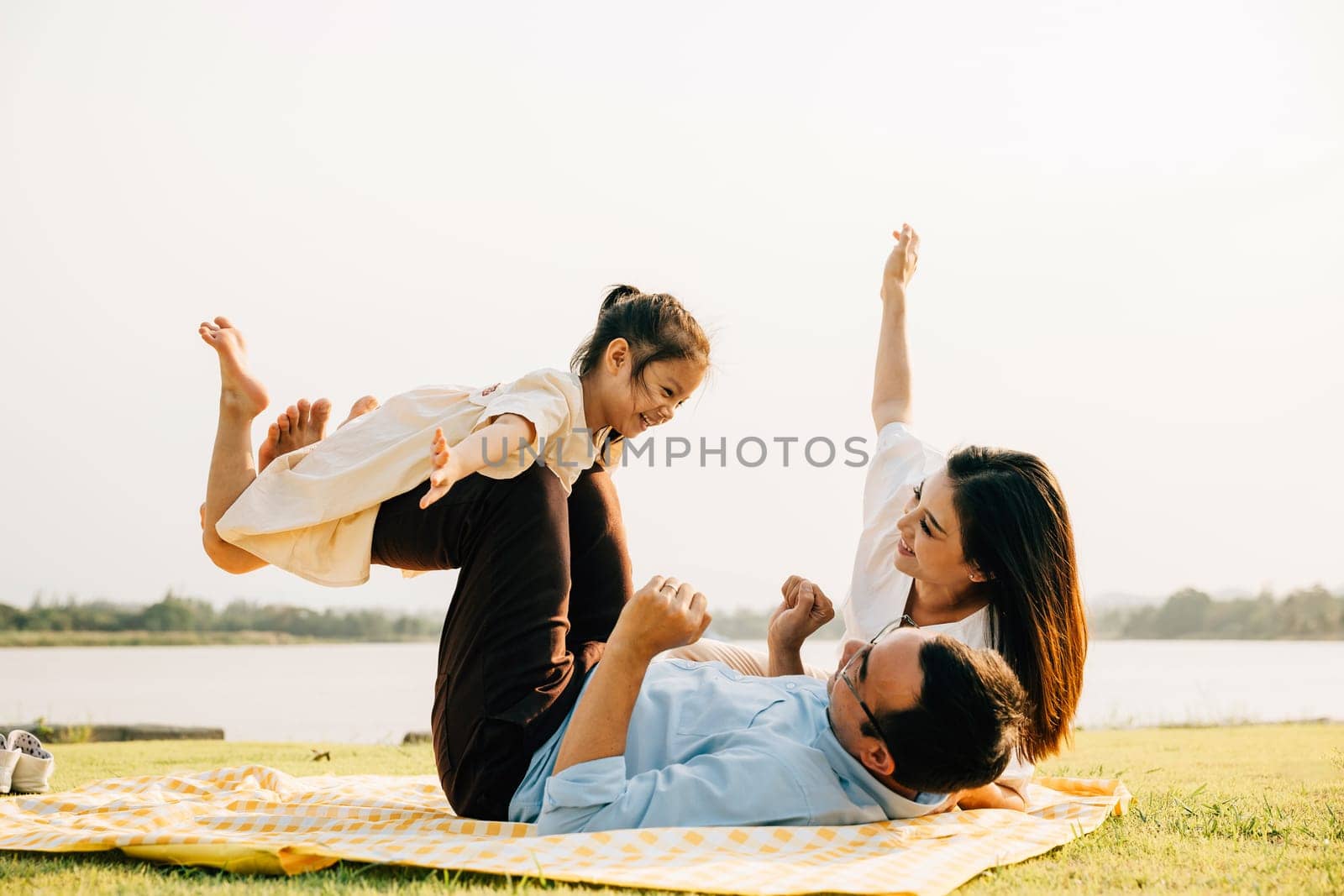 A family enjoys playful moments together. Father holds daughter high in air as she giggles and spreads her arms like wings, while mother watches with a smile outdoor. a precious moment of family fun