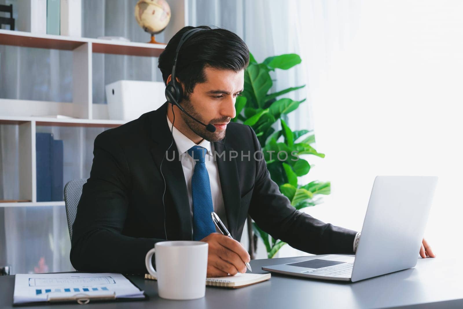 Male call center operator or telesales representative siting at his office desk wearing headset and engaged in conversation with client providing customer service support or making a sale. fervent