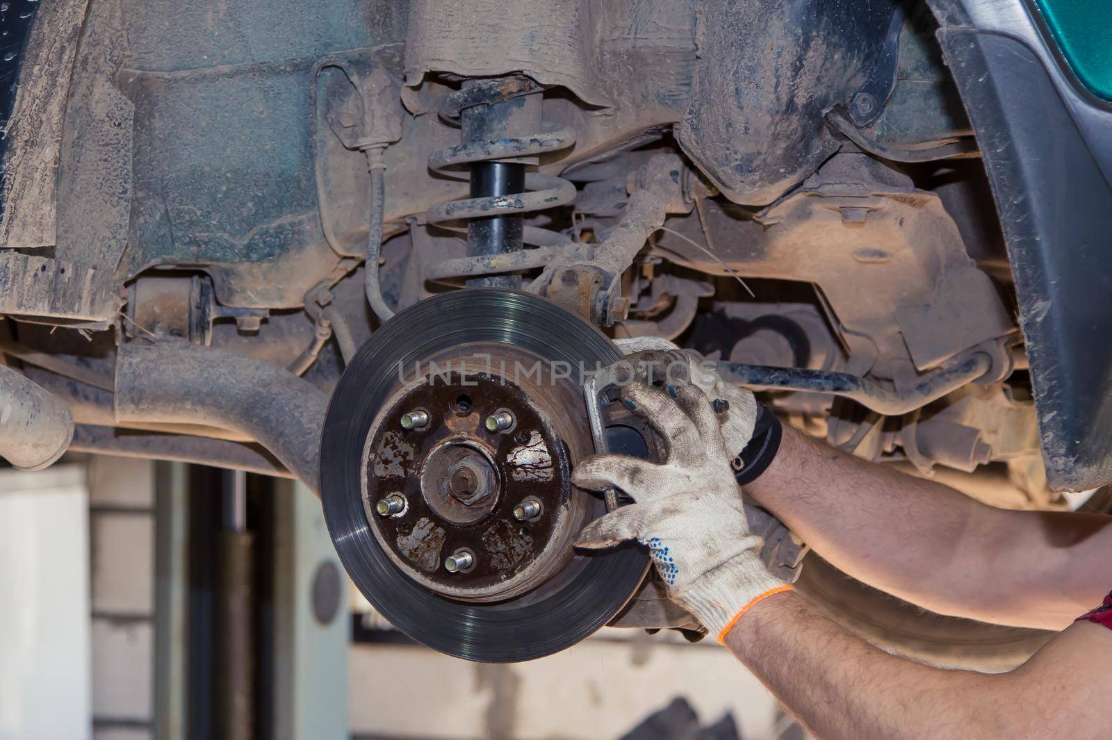 Gloved male hands install or remove the brake caliper of an old car. In the garage, a man changes parts on a vehicle. Small business concept, car repair and maintenance service. UHD 4K.