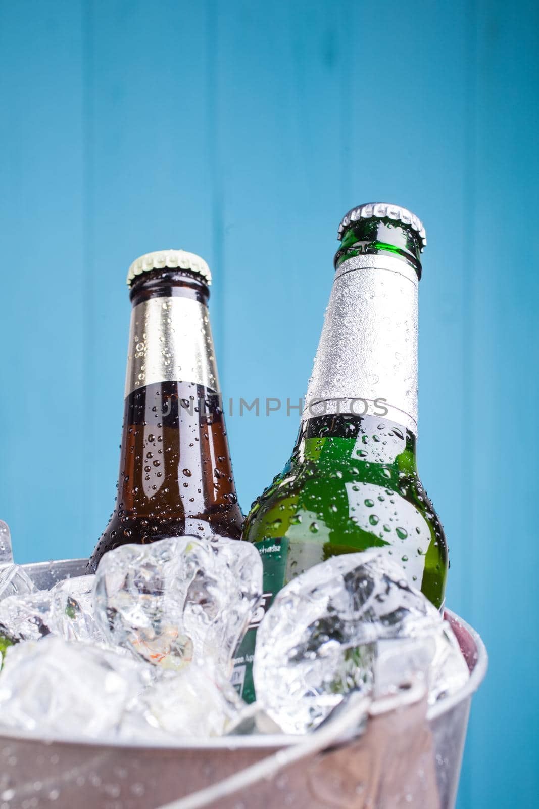 Three unopened bottles of beer inside metal bucket filled with iced