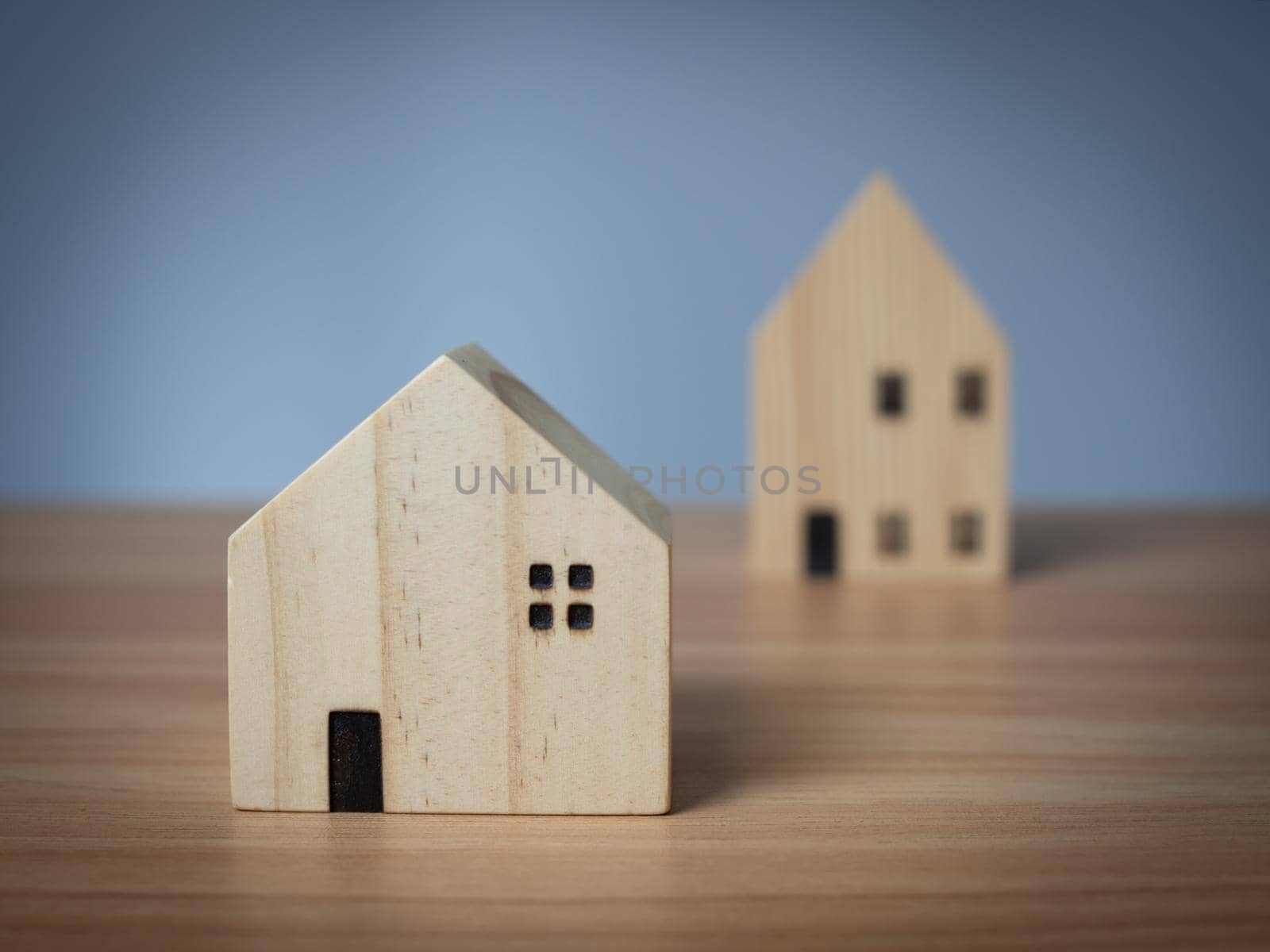 Two wooden model houses placed on a wooden table. with a light gray background