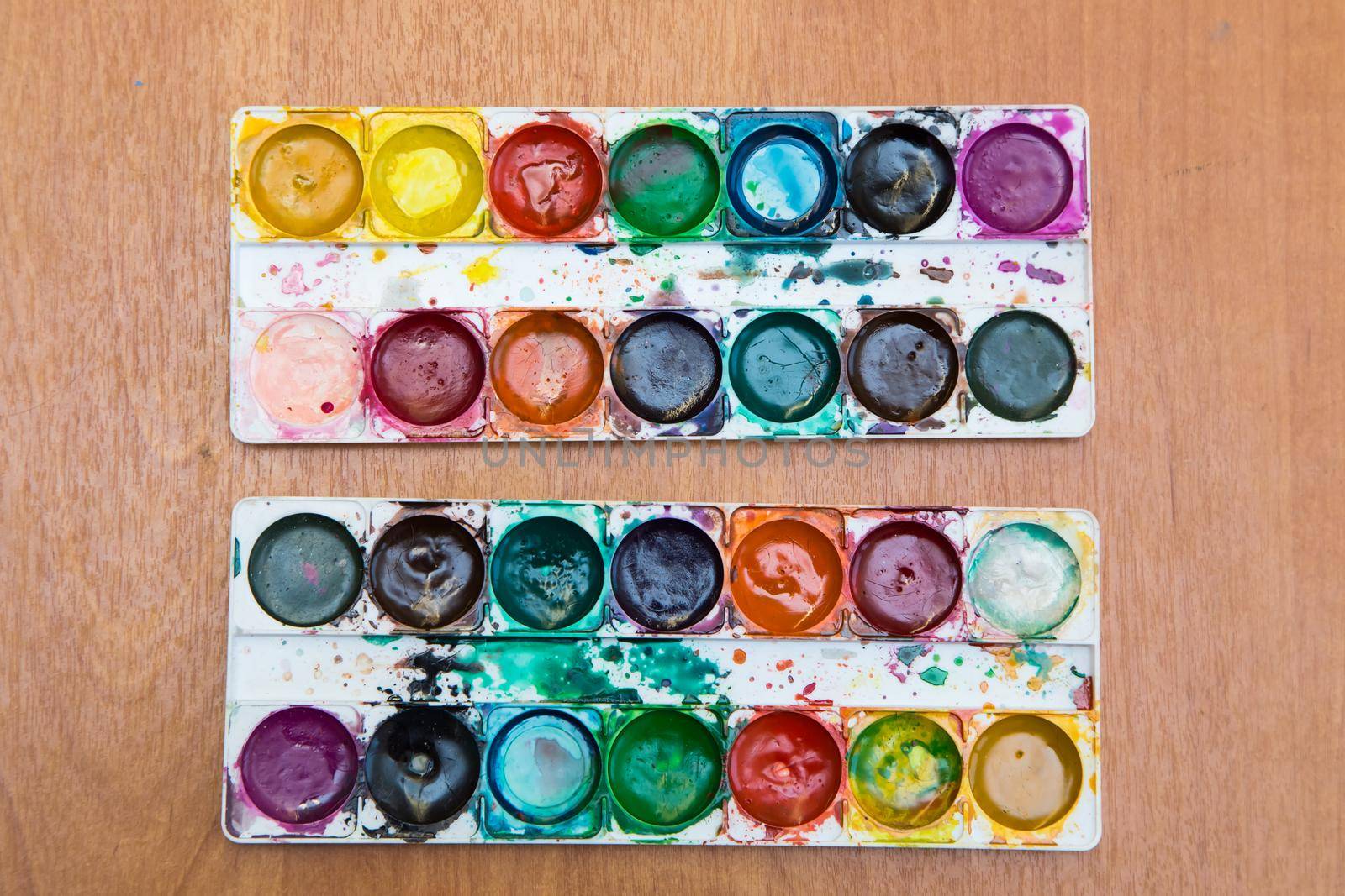 Two sets of multicolored watercolor paints used for painting. Top view of half-empty jars of watercolors. Flat layout on the table.