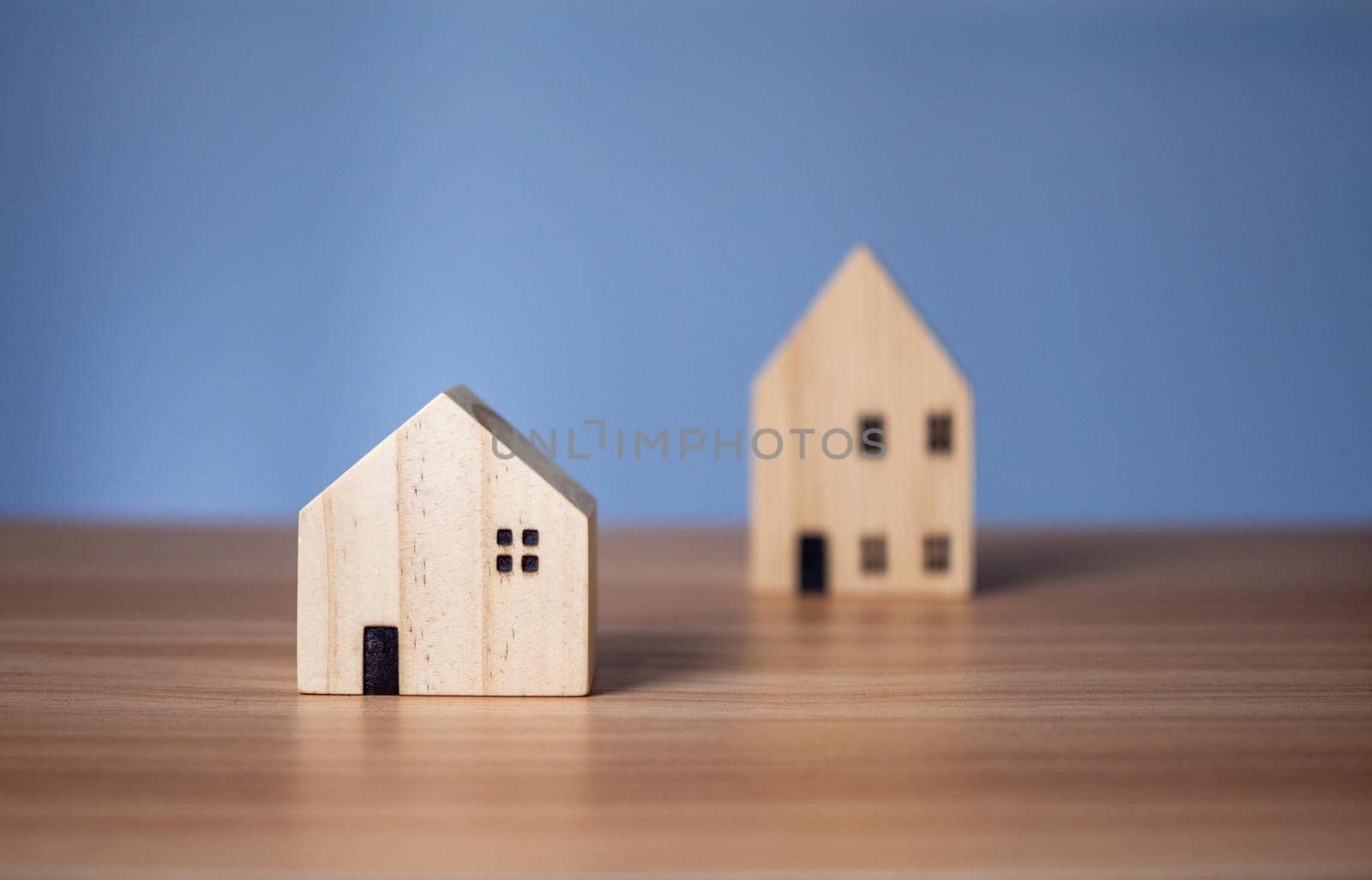 Two wooden model houses placed on a wooden table. with a light blue background