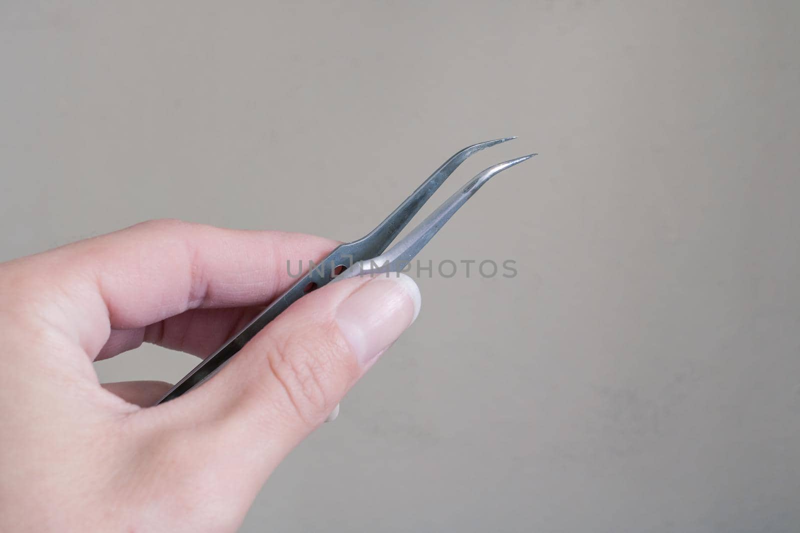 Tweezers in hand on a gray background close up