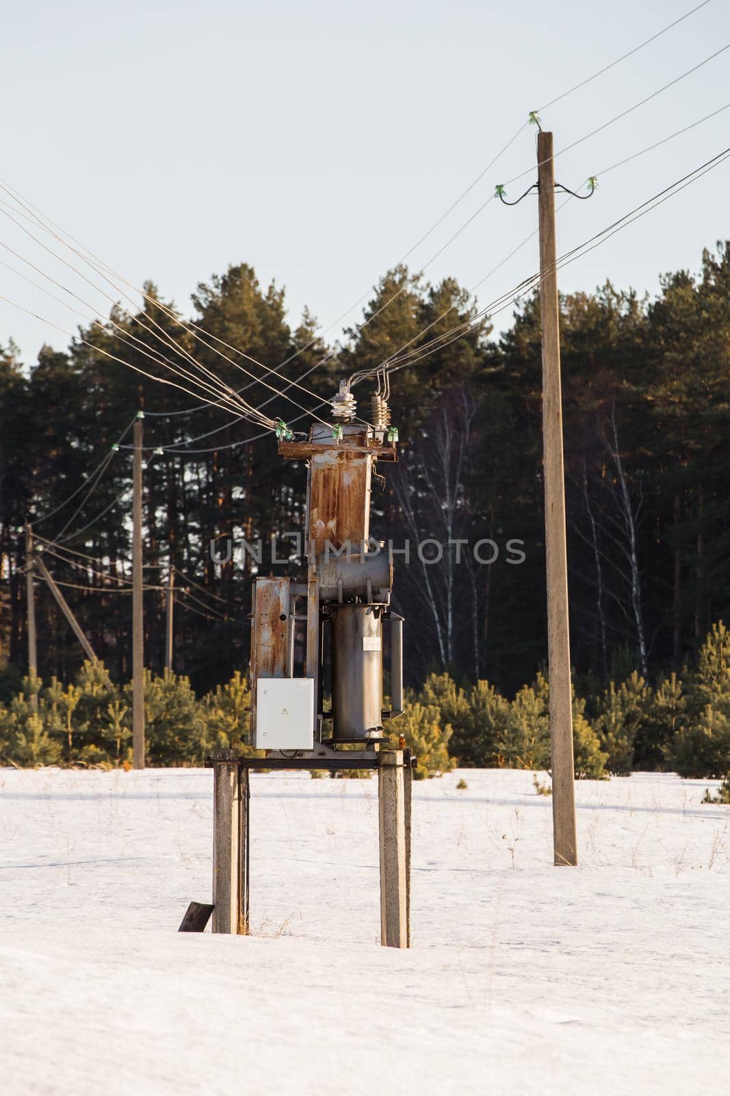 An impressive winter evening in nature, a transformer box in the field. The concept of power grids in the countryside. In the background there is a forest in the evening sunlight.