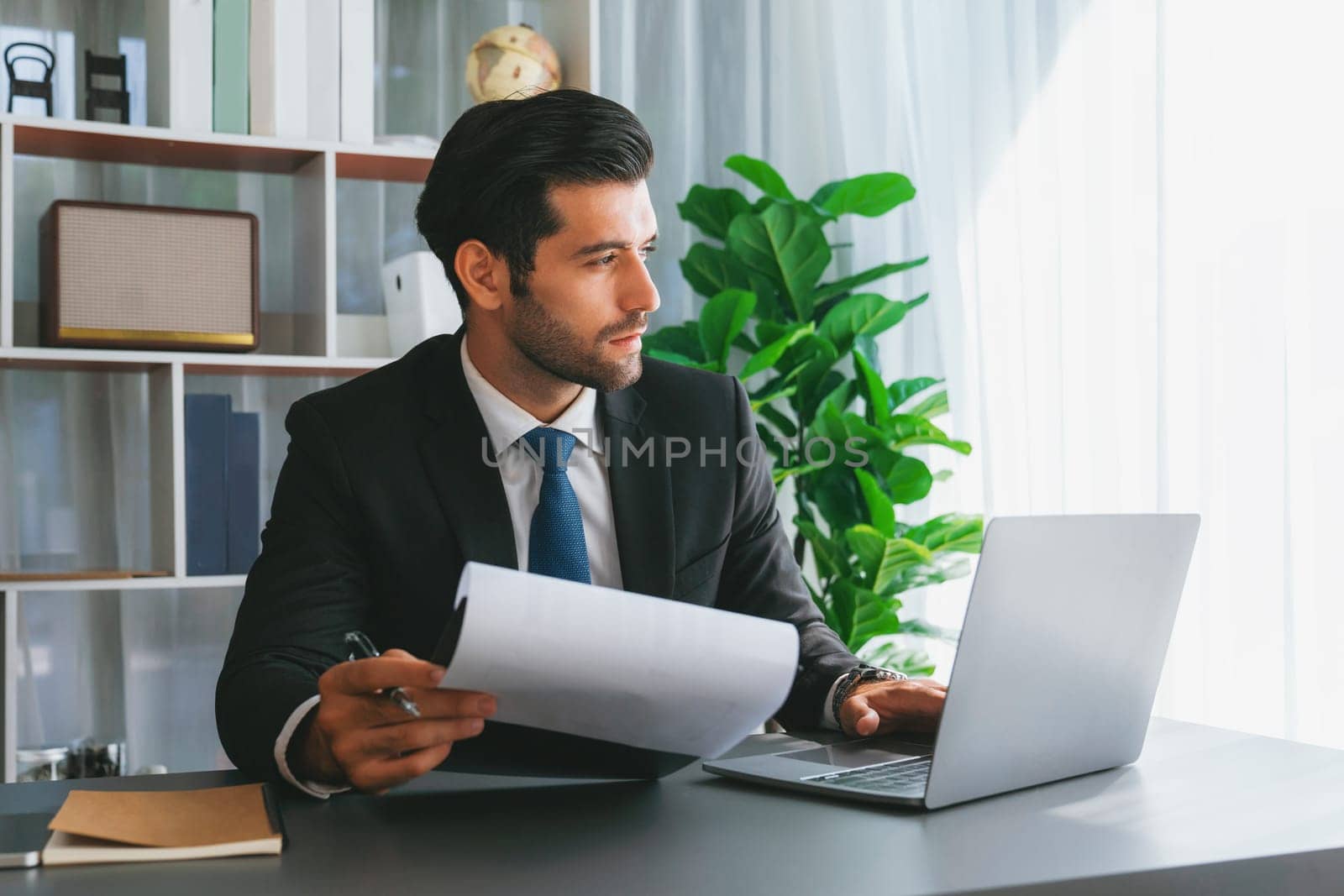 Modern professional businessman at modern office desk using laptop to work and write notes. Diligent office worker working on computer notebook in his office work space. fervent