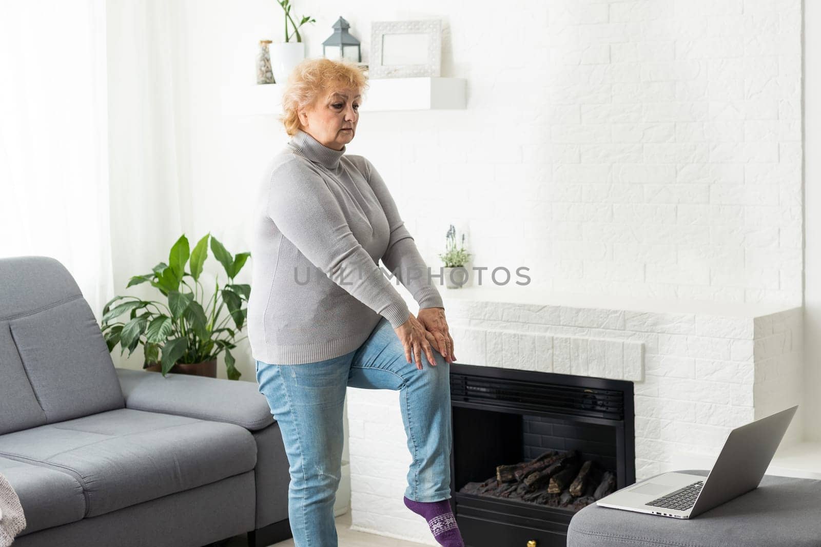 Training At Home. Sporty senior woman doing yoga plank while watching online tutorial on laptop, exercising in living room, free space, panorama by Andelov13