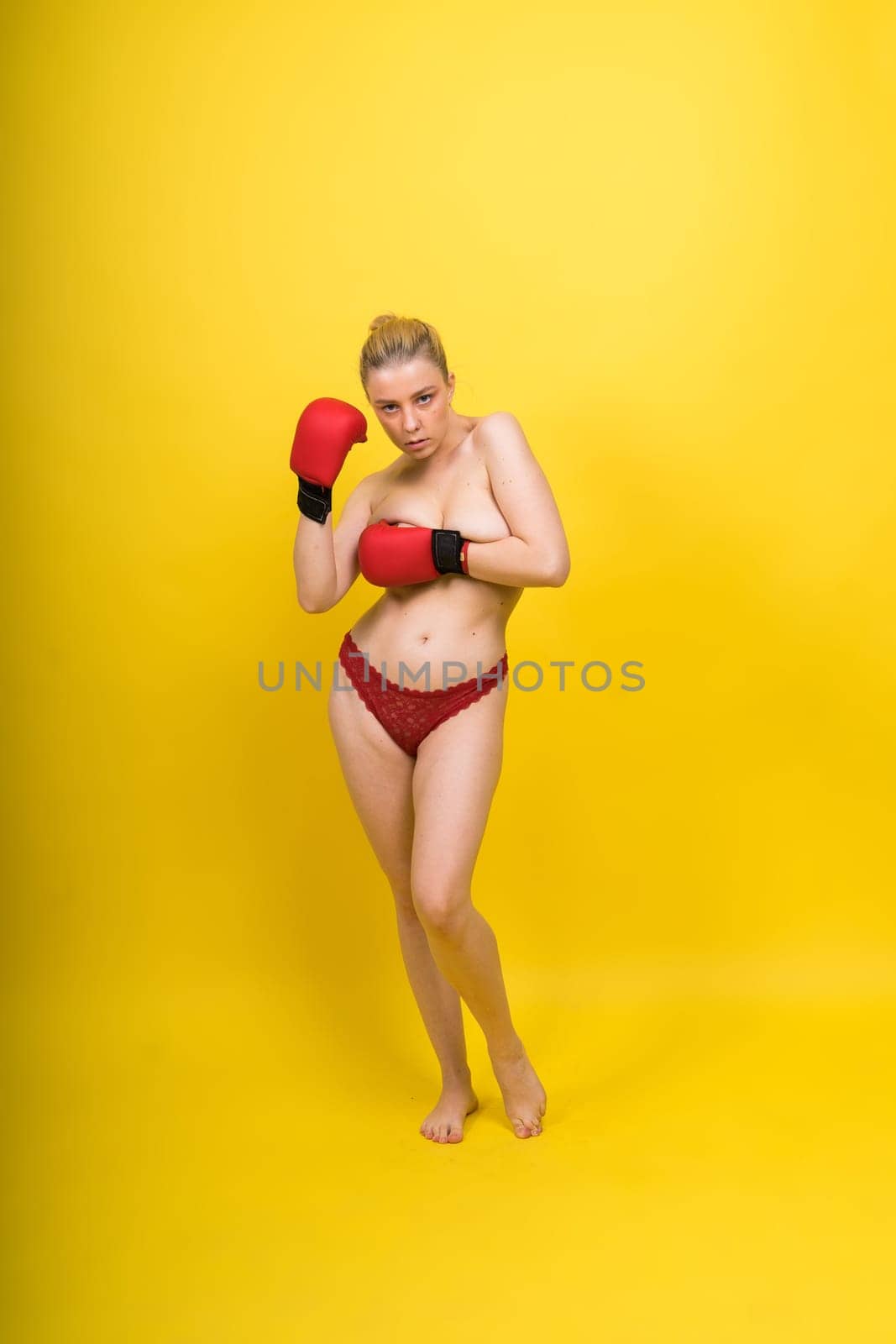 Seductive young and fit female fighter posing in gloves in a studio