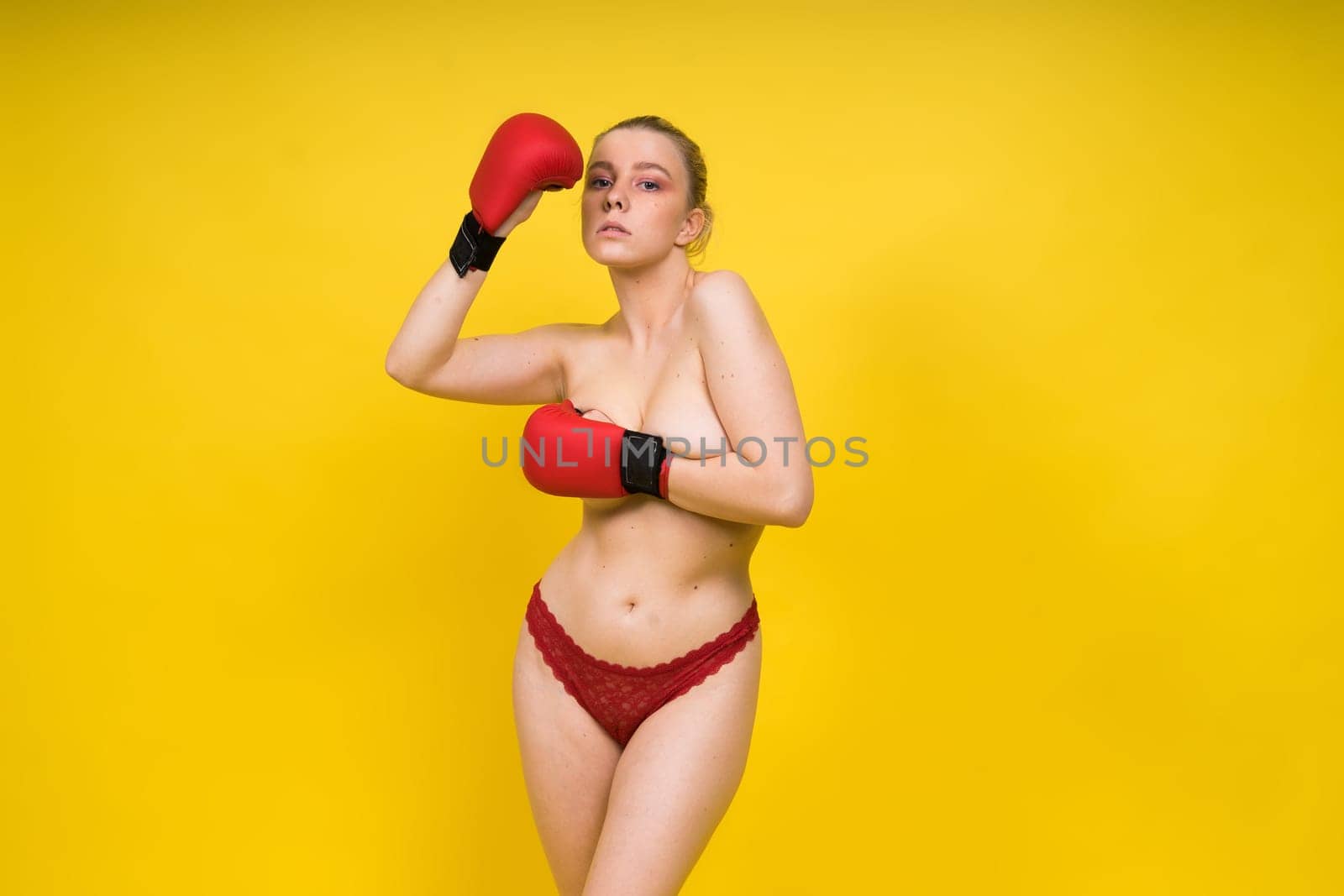 Seductive young and fit female fighter posing in gloves in a studio