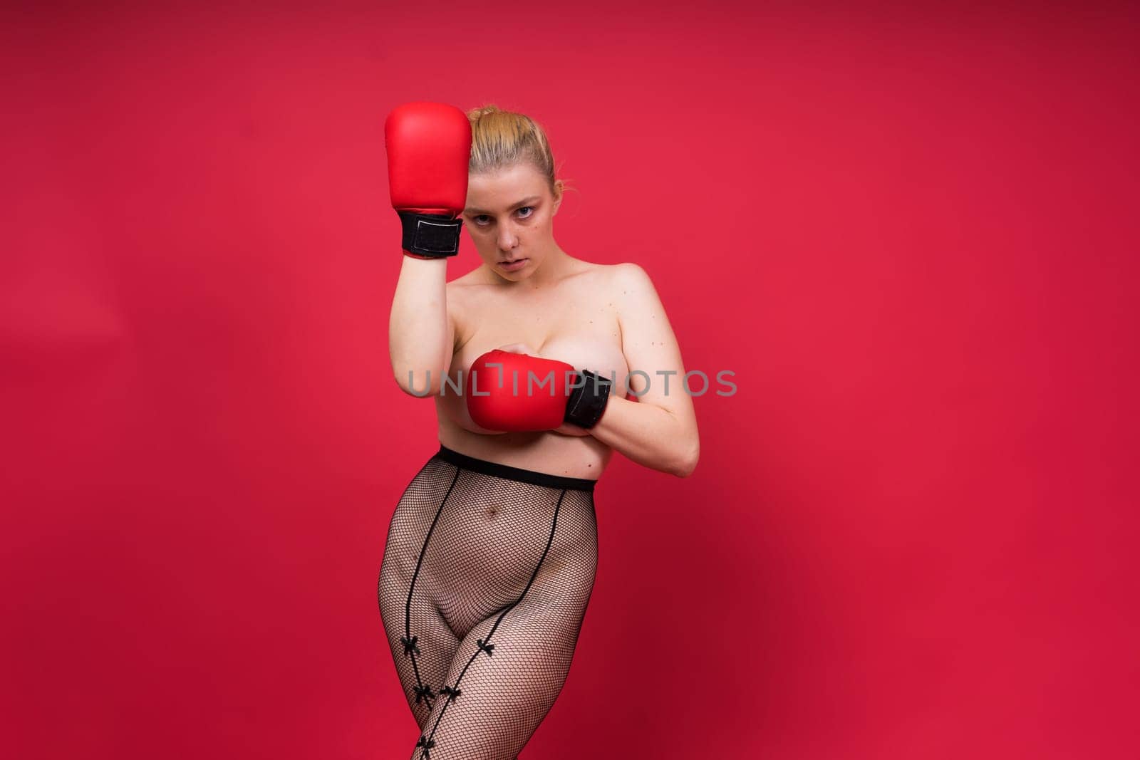Seductive young and fit female fighter posing in gloves in a studio