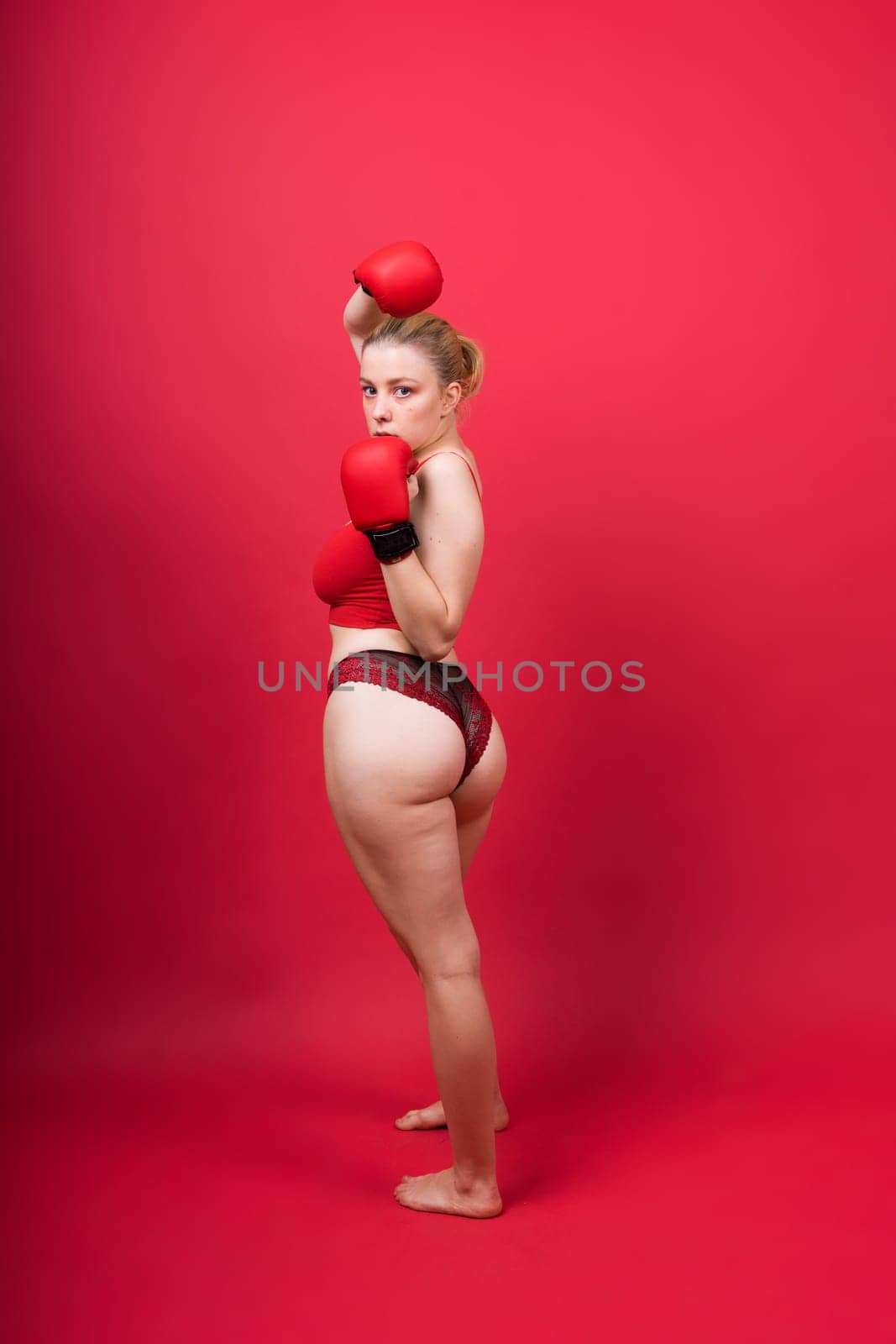 Seductive young and fit female fighter posing in gloves in a studio