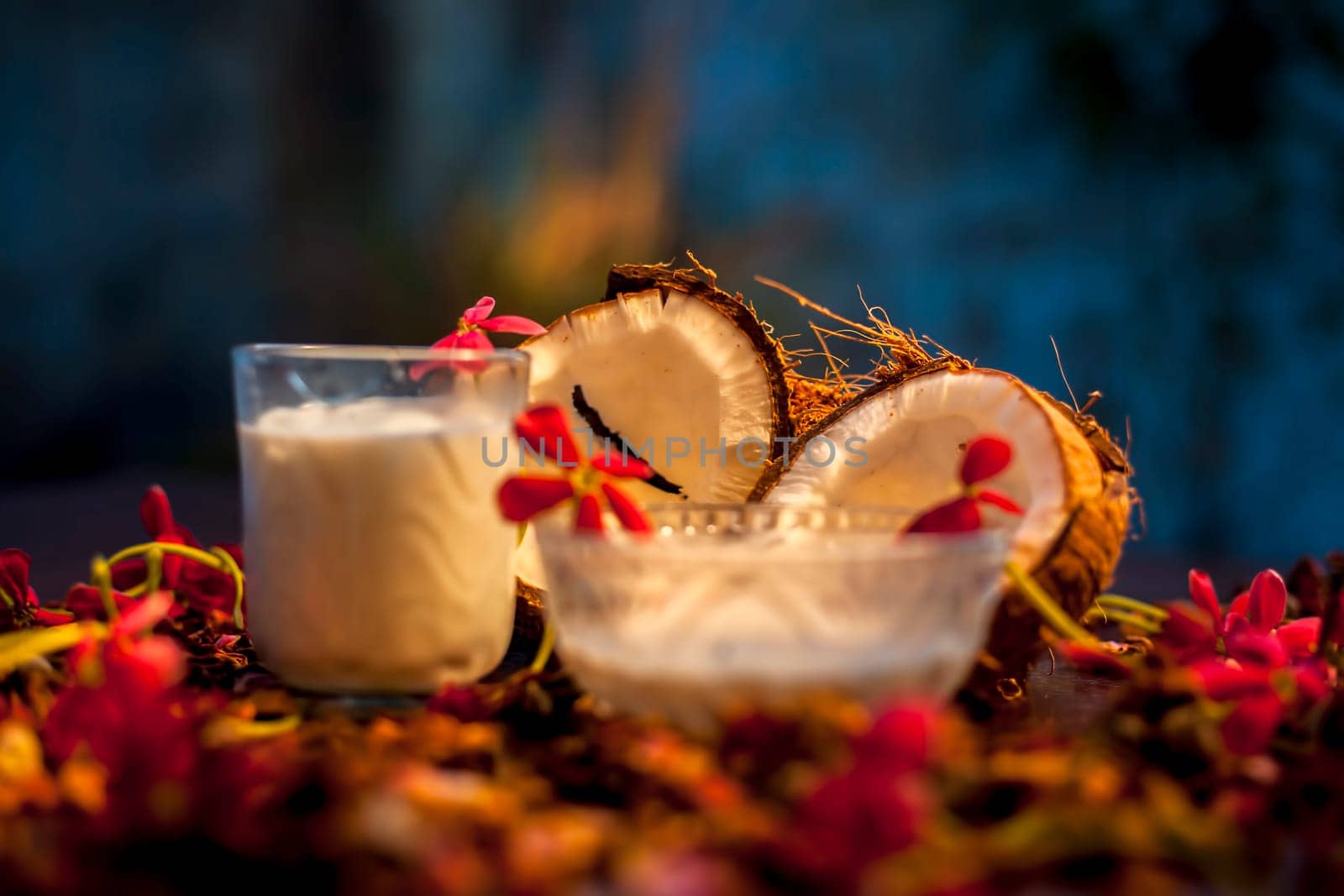 Coconut face mask consisting of coconut milk and yogurt for flawless skin and to moisturize it. Shot of raw coconut cut coconut, milk, and yogurt with some flowers spread on the brown wooden surface. by mirzamlk