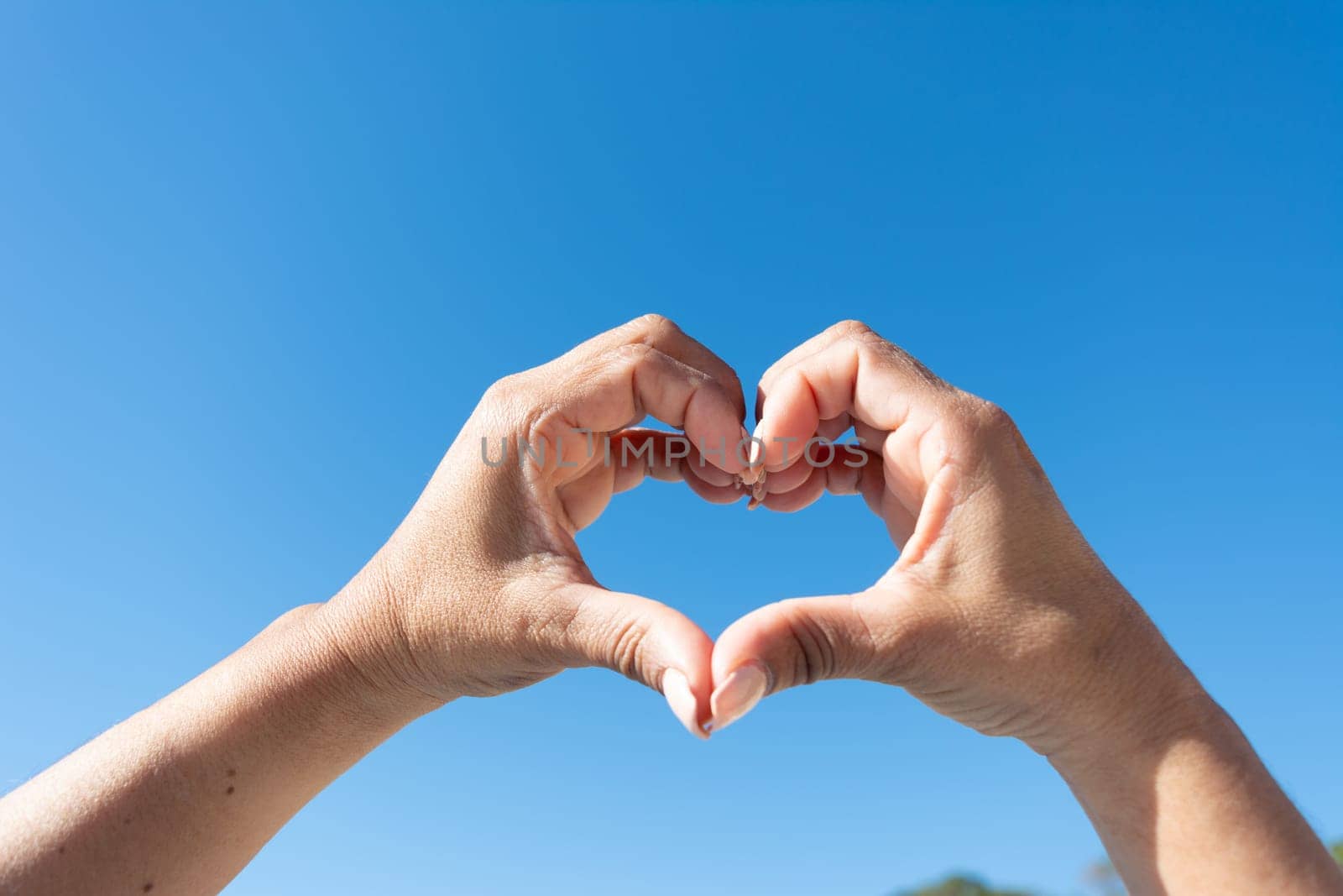 woman's hands showing heart sign on blue sky background,