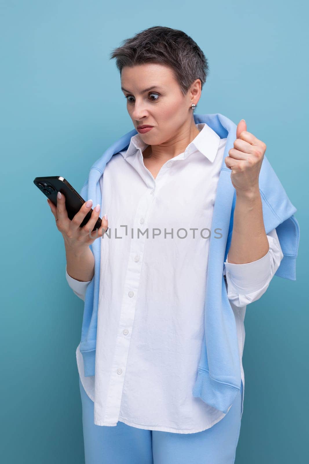 excited young woman with short haircut using smartphone on blue background.