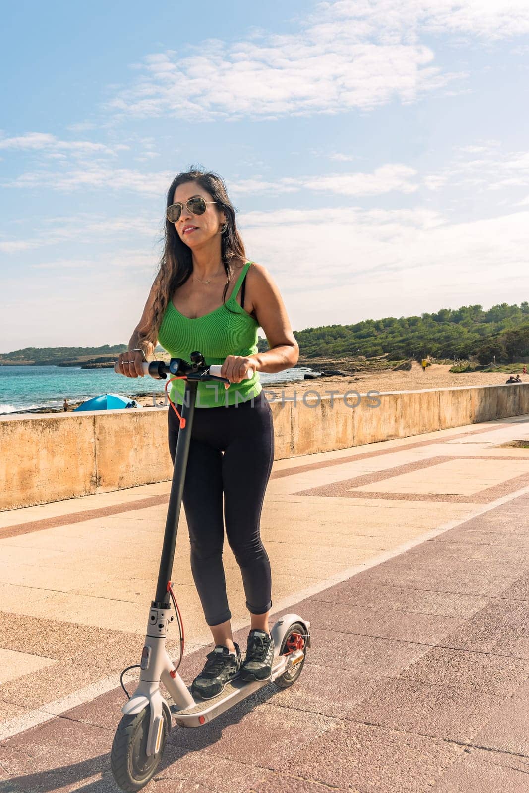 Woman riding electric scooter, happy and summer ride at tropical island beach resort for vacation. City, street and eco friendly transport, fun on escooter on holiday in mallorca,balearic island by carlosviv