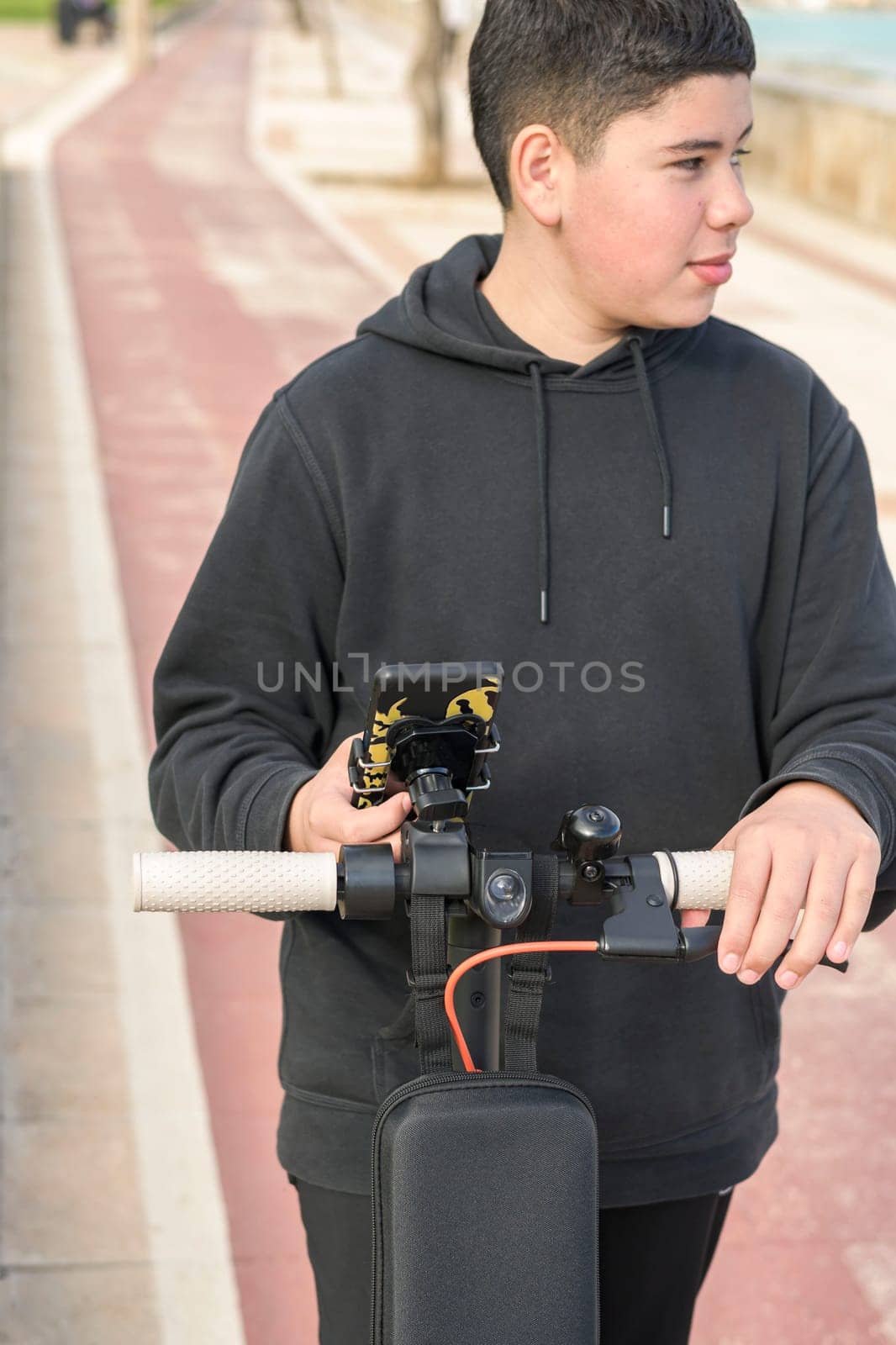 young teenager with a sideways glance riding an electric skateboard and using a smartphone application by carlosviv