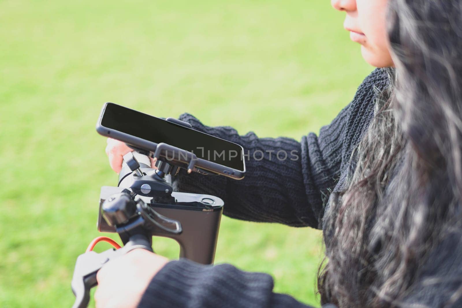 side view of Beautiful Latina woman with long black hair riding her motorised scooter in the city, using smart phone app, mobility concept sustainable transport, zero CO2 emissions Emobility