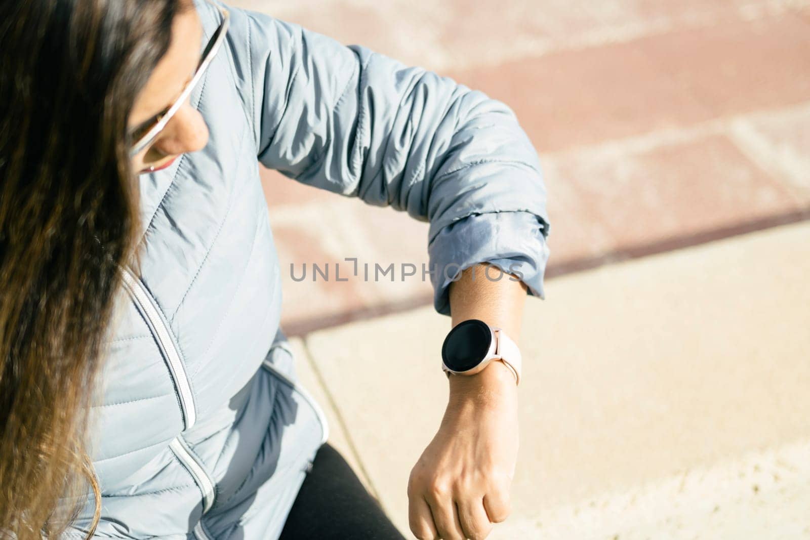 latin woman with long hair looking at smartwatch wearing sunglasses and blue jacket, wireless technology social media concept
