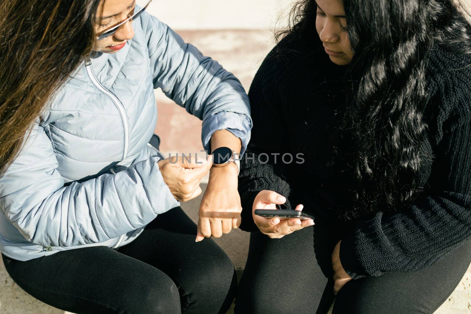 two beautiful long hair latin women synchronizing data on smart phone and smart watch, shopping on the net, internet shopping concept