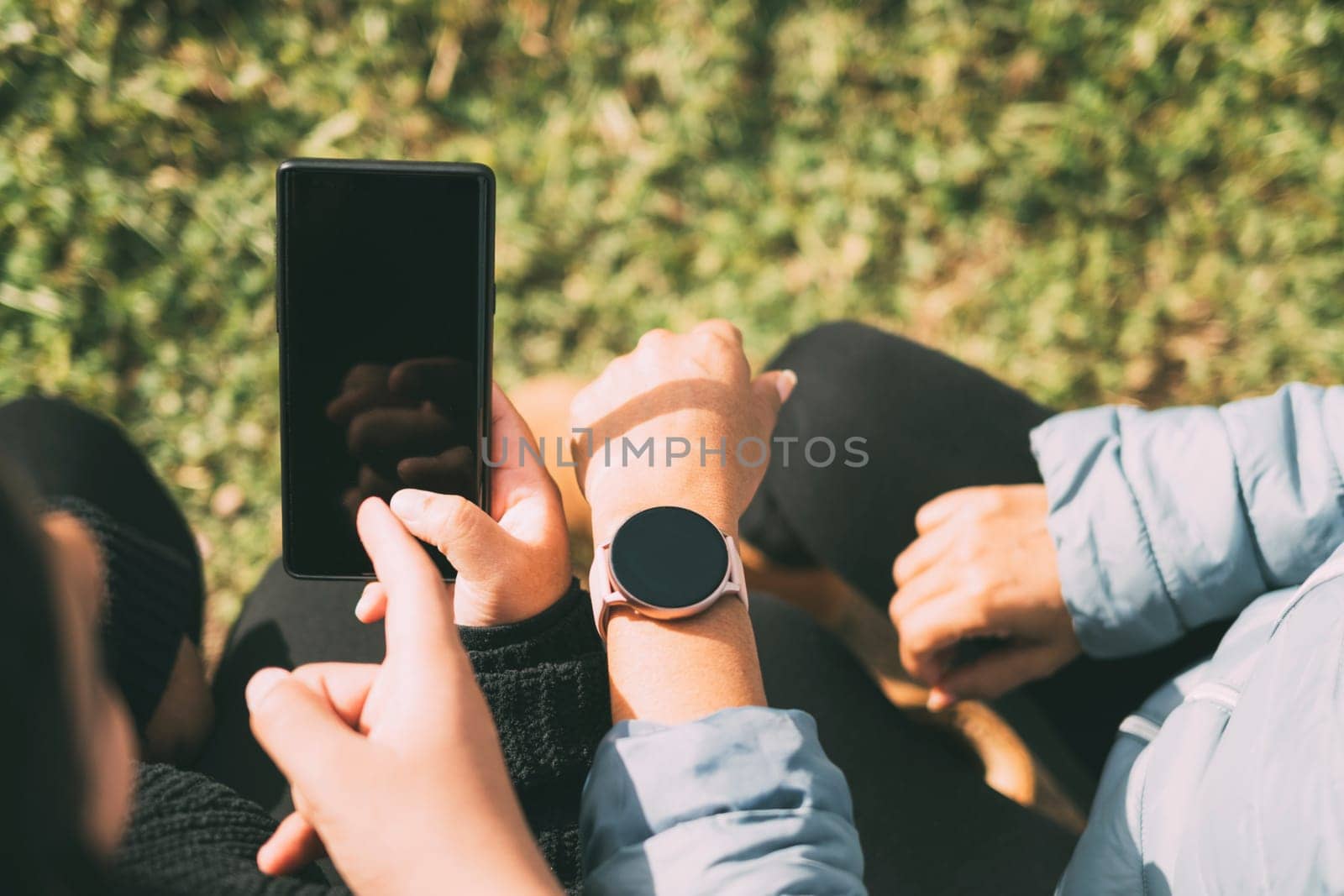 Hispanic male teenager holding smartphone looking away while sitting on grass with Hispanic mother and sister in park on sunny day,