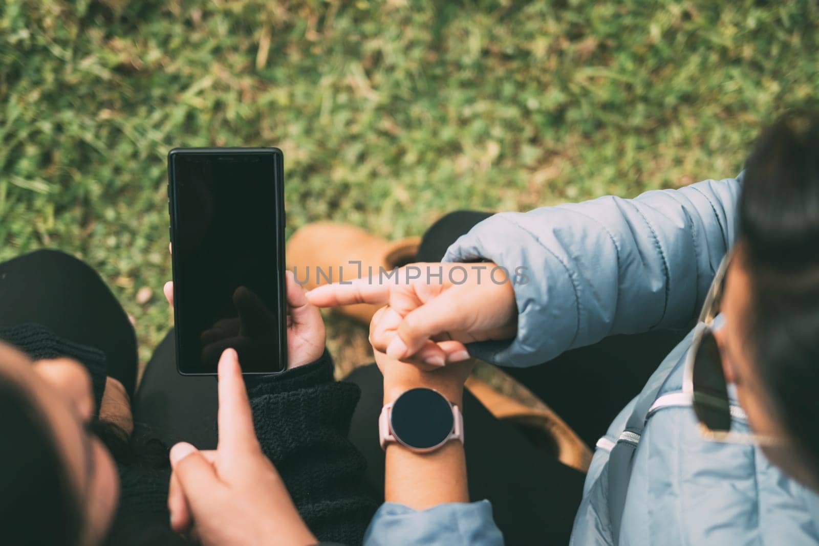 Cropped hands of a woman with a smart watch, pointing to a smartphone, concept of technology, social networking, with two people indicating something on the smartphone.