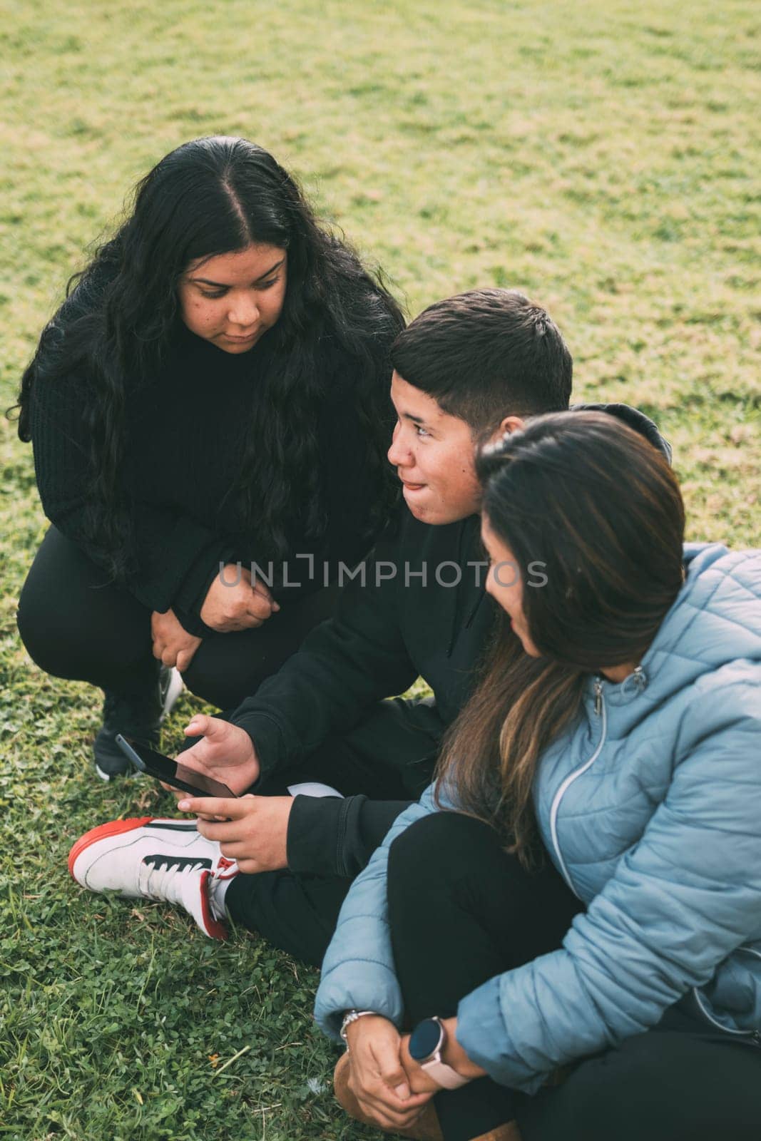 happy family in the park sitting, watching and sharing smartphones by carlosviv
